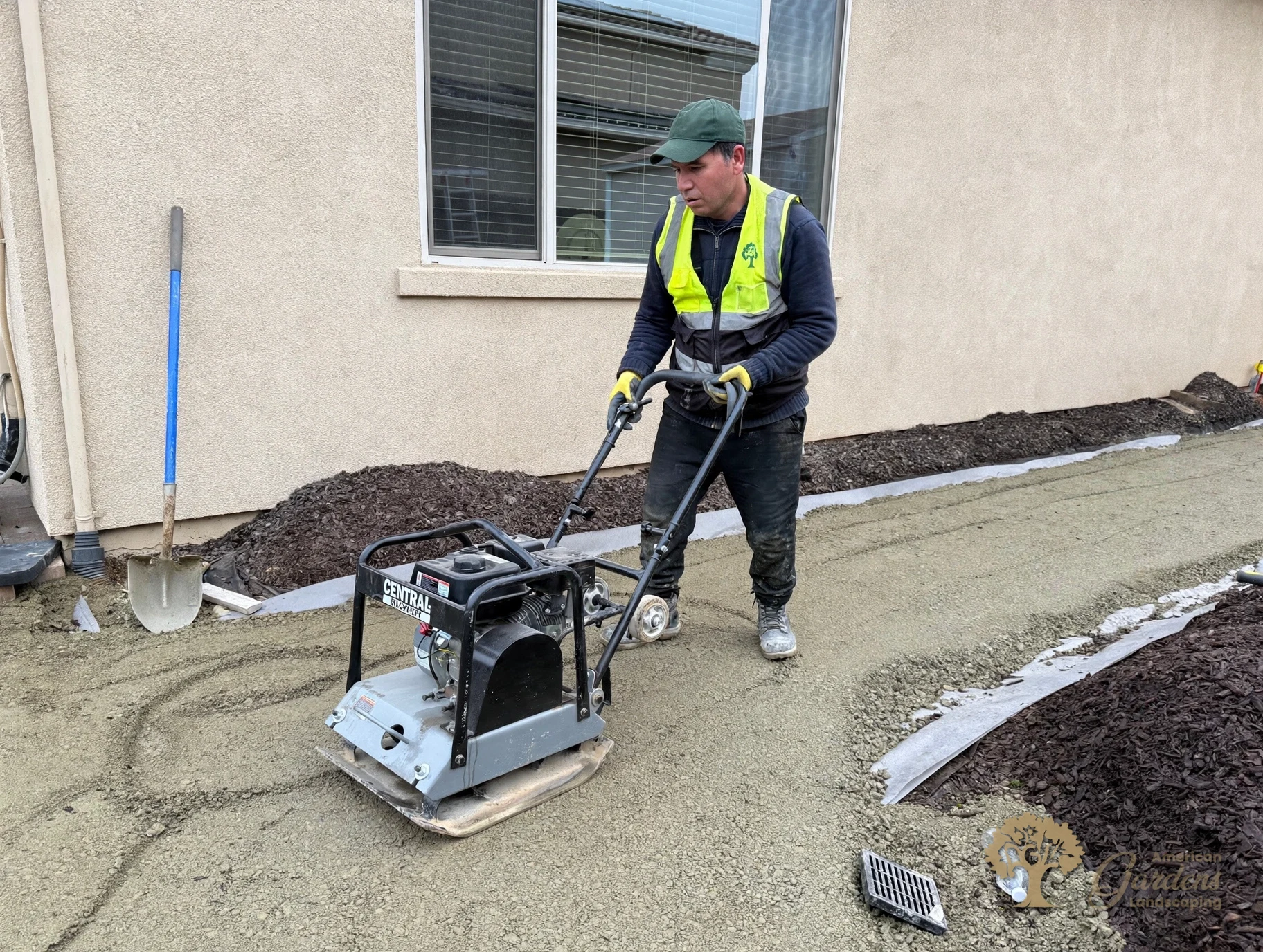 Crew member running a plate compactor over the sand base to lock it in before the pavers go down, in El Dorado Hills, by American Gardens Landscaping.