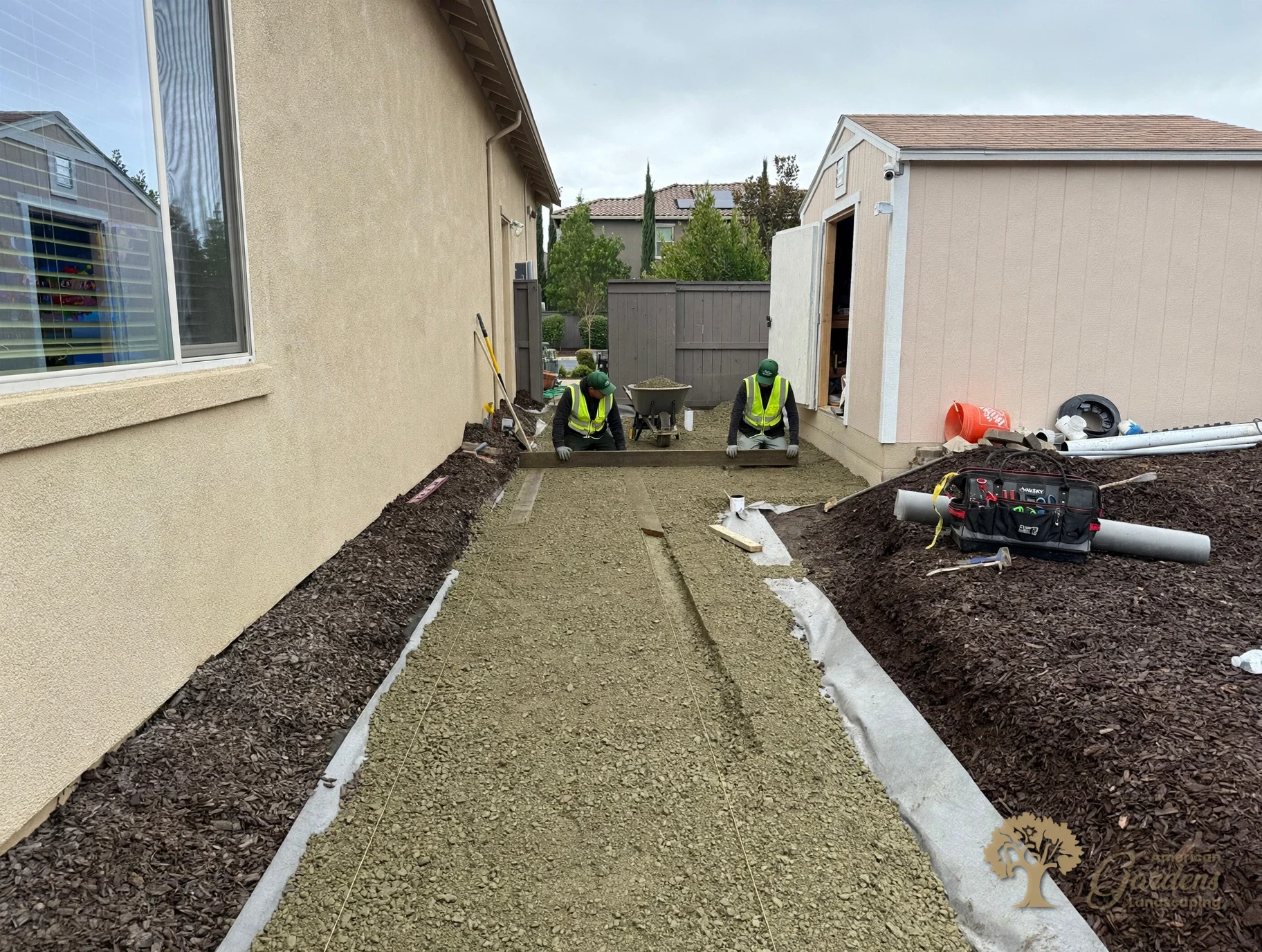Two American Gardens Landscaping crew members screeding the base level between the house and the shed for a new paver patio in El Dorado Hills.
