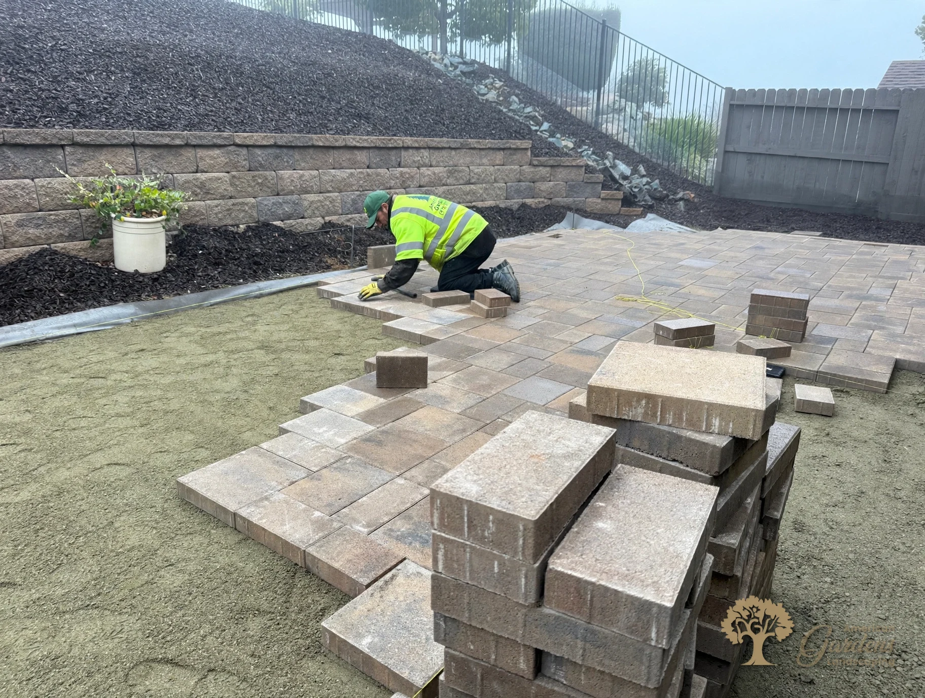 American Gardens Landscaping crew member laying pavers by hand on the sand bed at the base of the block retaining wall in El Dorado Hills.