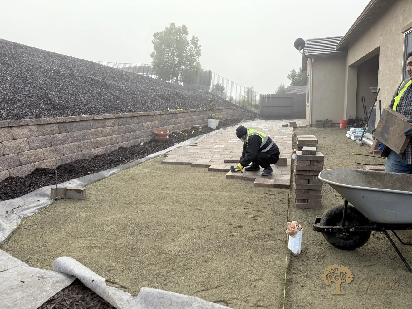 Crew member tapping each paver into place with a rubber mallet while the next pavers are carried in, during a patio installation in El Dorado Hills.