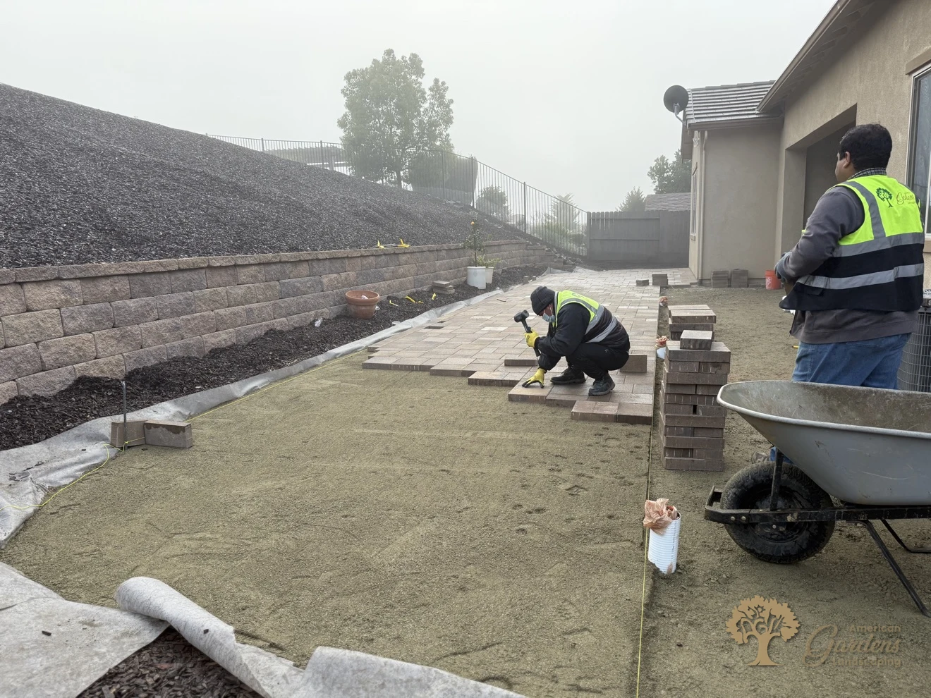 American Gardens Landscaping crew laying pavers across the yard, with the branded uniform vest visible, in El Dorado Hills.