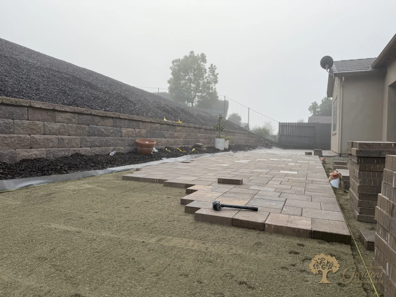 Paver patio halfway laid, with stacks of pavers and the rubber mallet on the finished section, in El Dorado Hills, by American Gardens Landscaping.