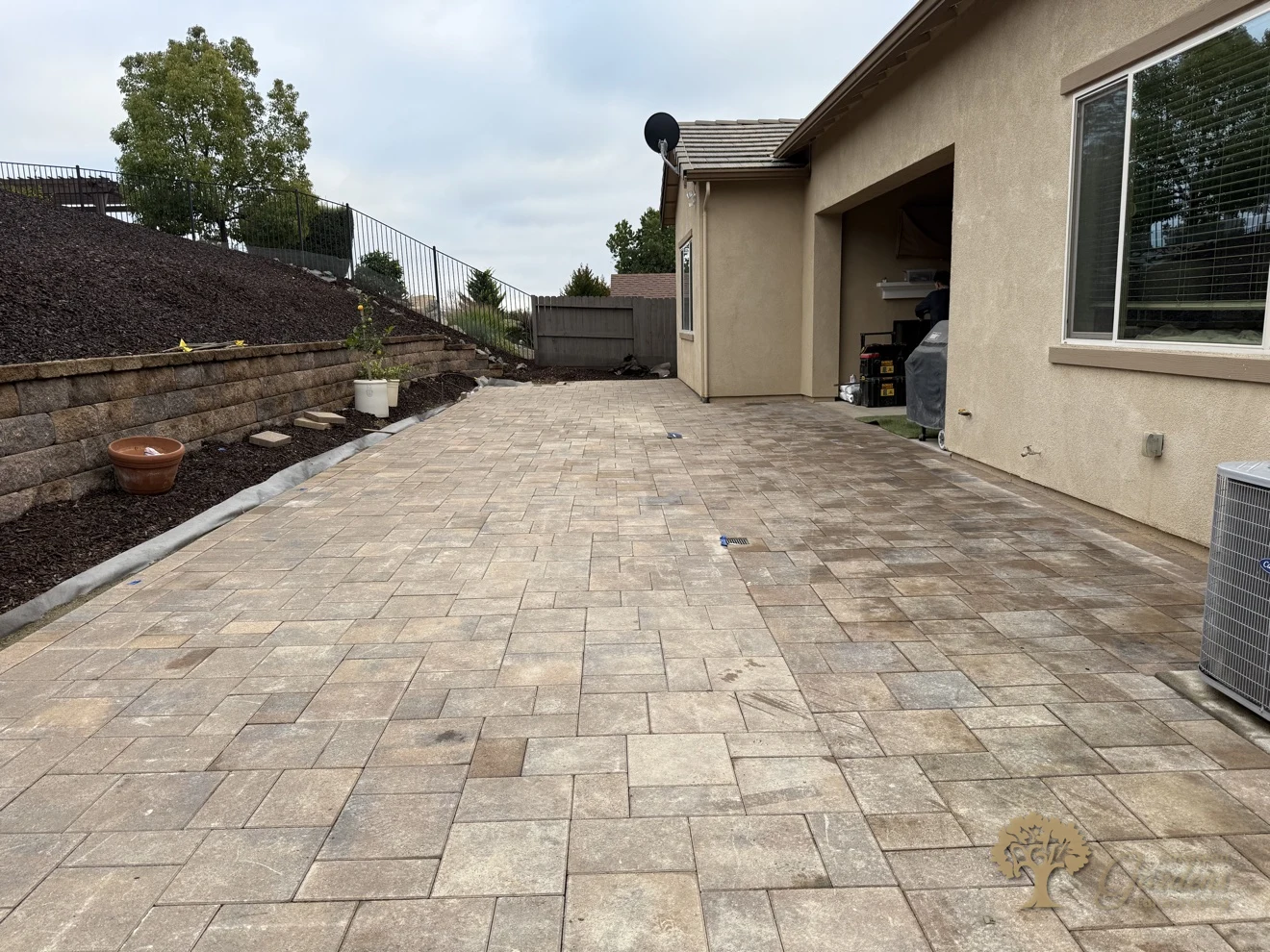 Finished paver patio running the length of the house below the block retaining wall and bark slope in El Dorado Hills, by American Gardens Landscaping.