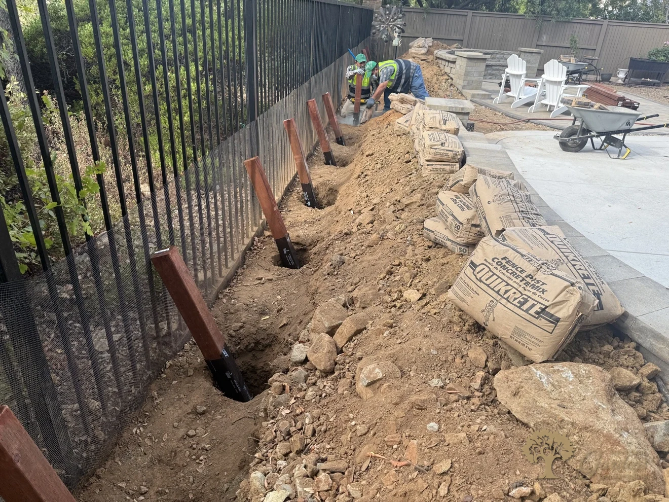 A line of deep post holes with black-wrapped fence posts and concrete mix ready along a metal fence in El Dorado Hills' Serrano neighborhood, by American Gardens Landscaping.