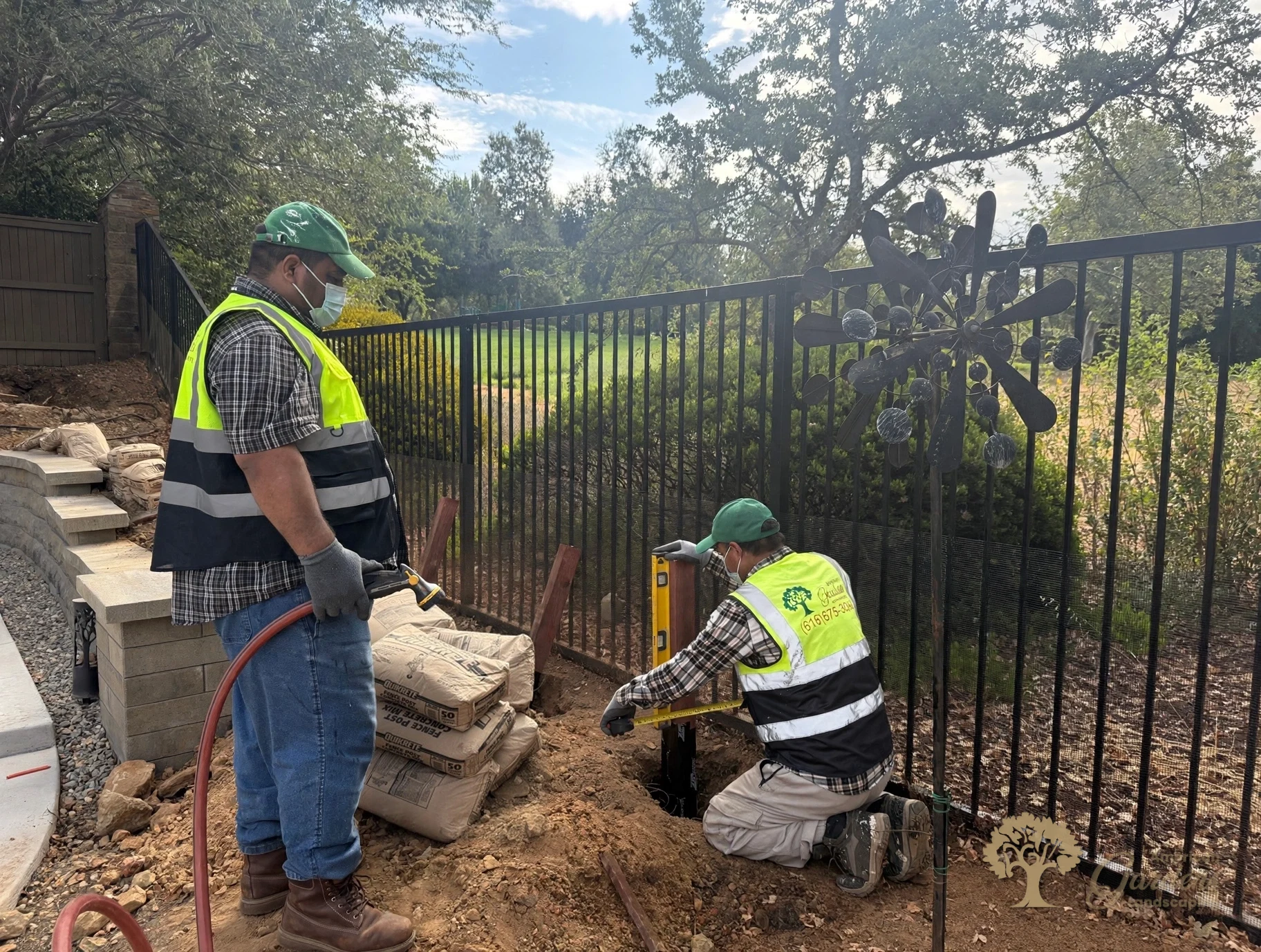 Crew leveling a wrapped fence post as concrete is mixed, with the company vest and phone number visible, in El Dorado Hills' Serrano neighborhood, by American Gardens Landscaping.