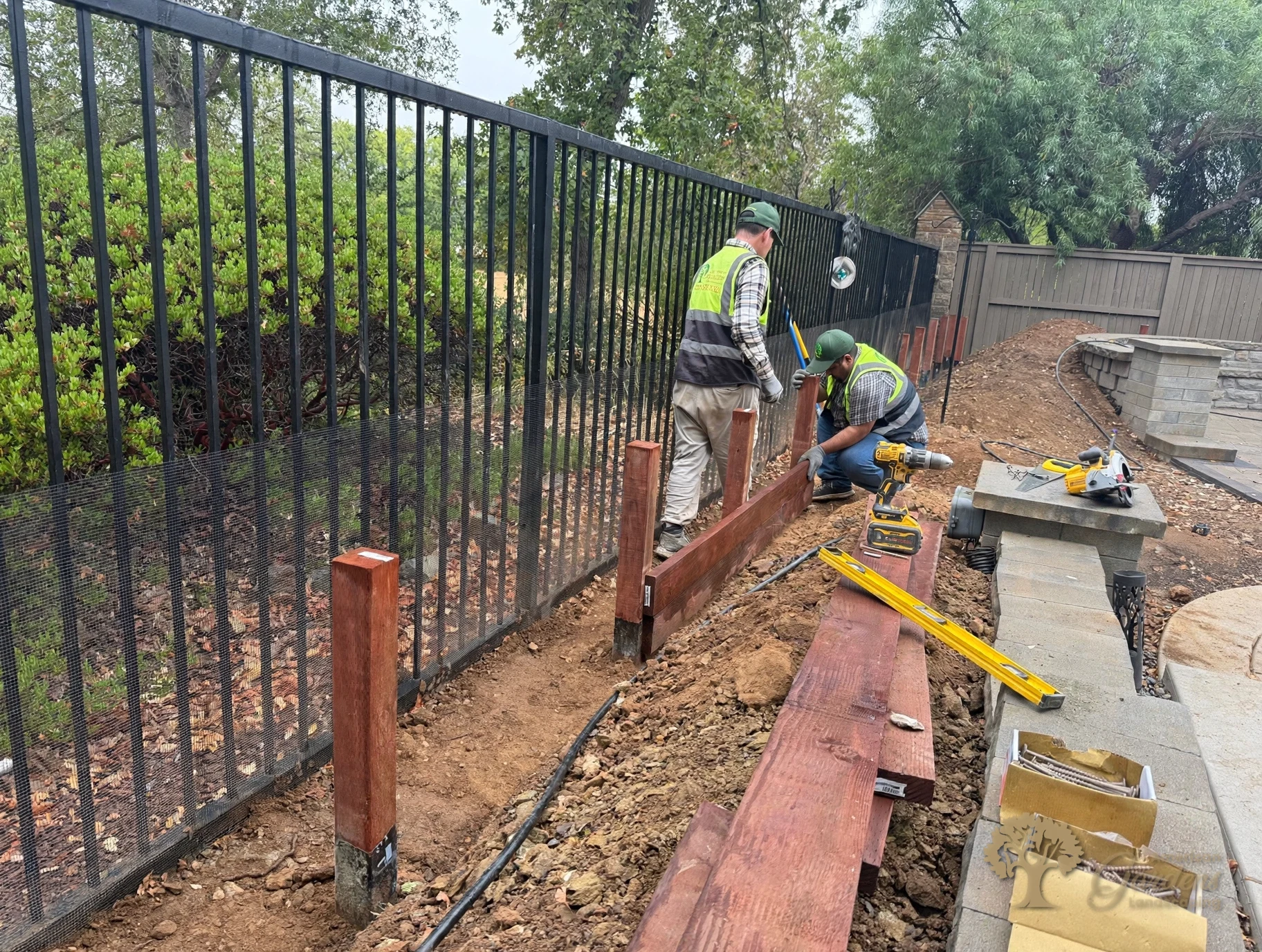 Crew fitting the first stained board onto new fence posts with wrapped bases along a metal view fence in El Dorado Hills, by American Gardens Landscaping.