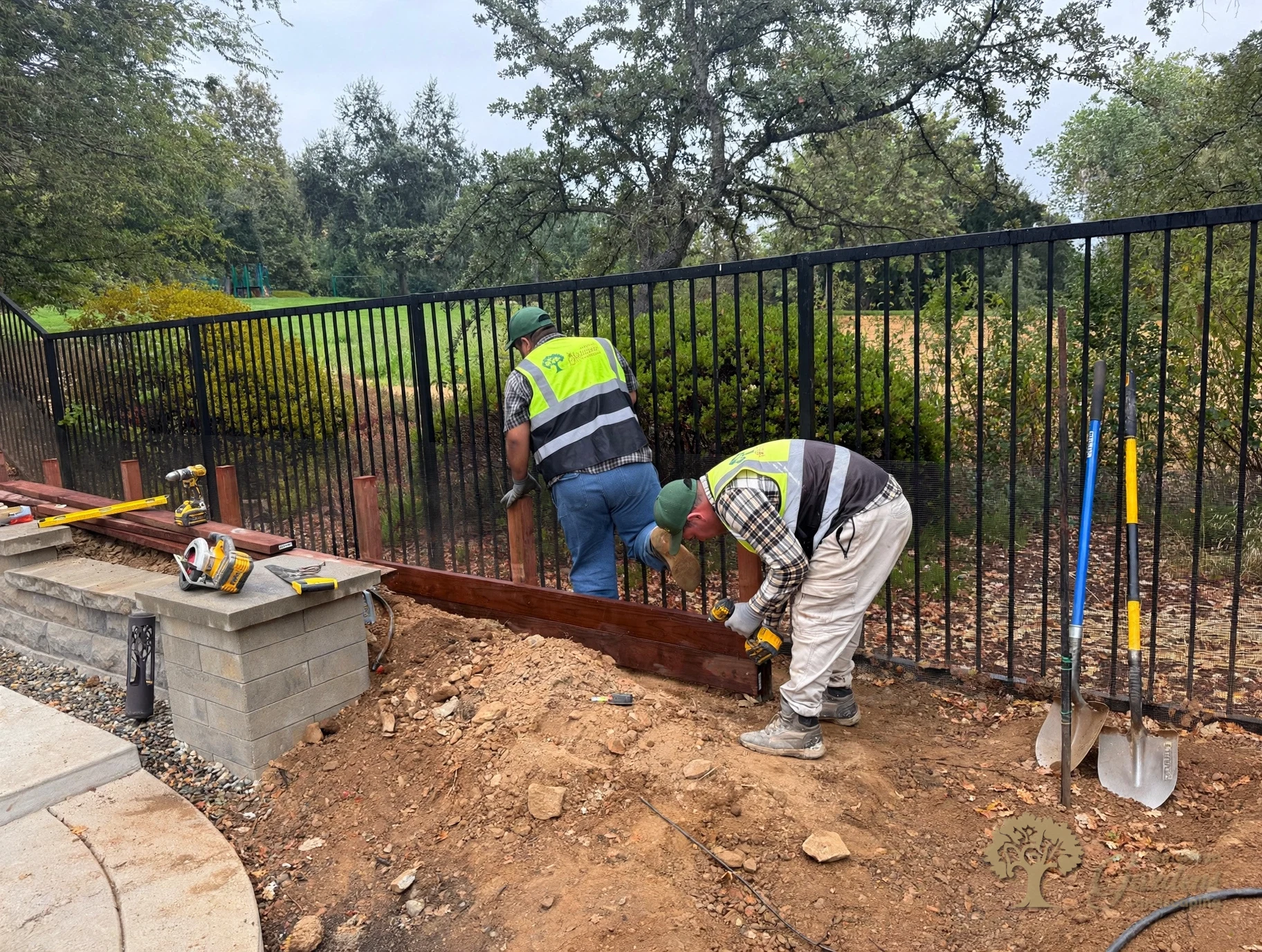Crew fastening a stained kick board to new posts at the base of a black metal fence in Serrano, El Dorado Hills, by American Gardens Landscaping.