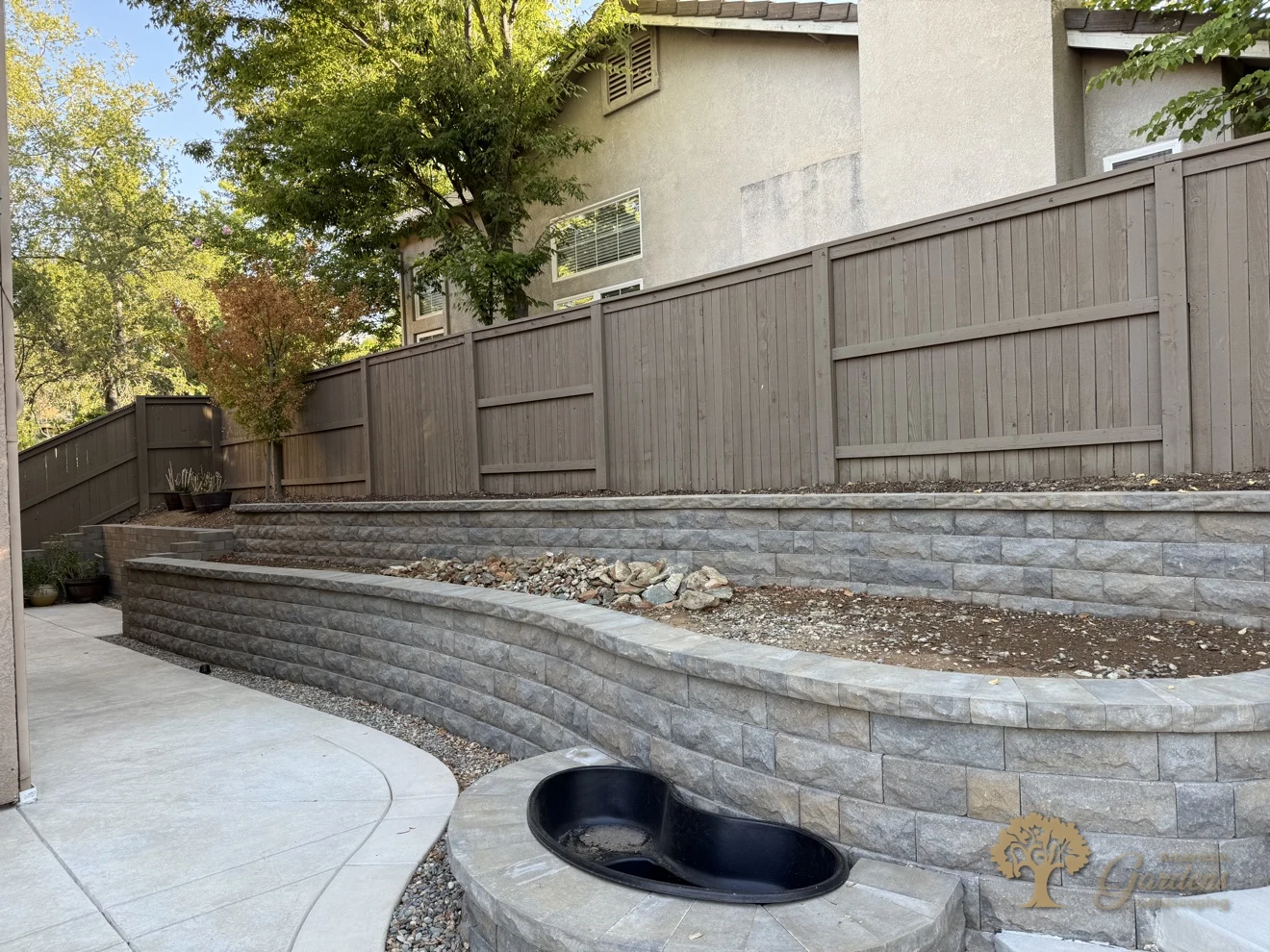 Terraced block retaining walls with a kidney-shaped pond basin and concrete patio in a Serrano backyard in El Dorado Hills, by American Gardens Landscaping.