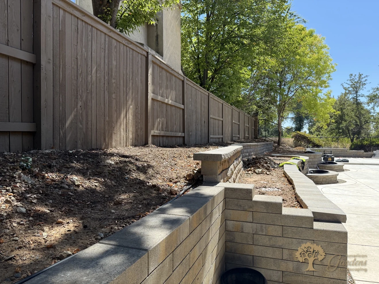 Long view of new block retaining walls and terraced planting beds below a stained wood fence in El Dorado Hills' Serrano neighborhood, by American Gardens Landscaping.