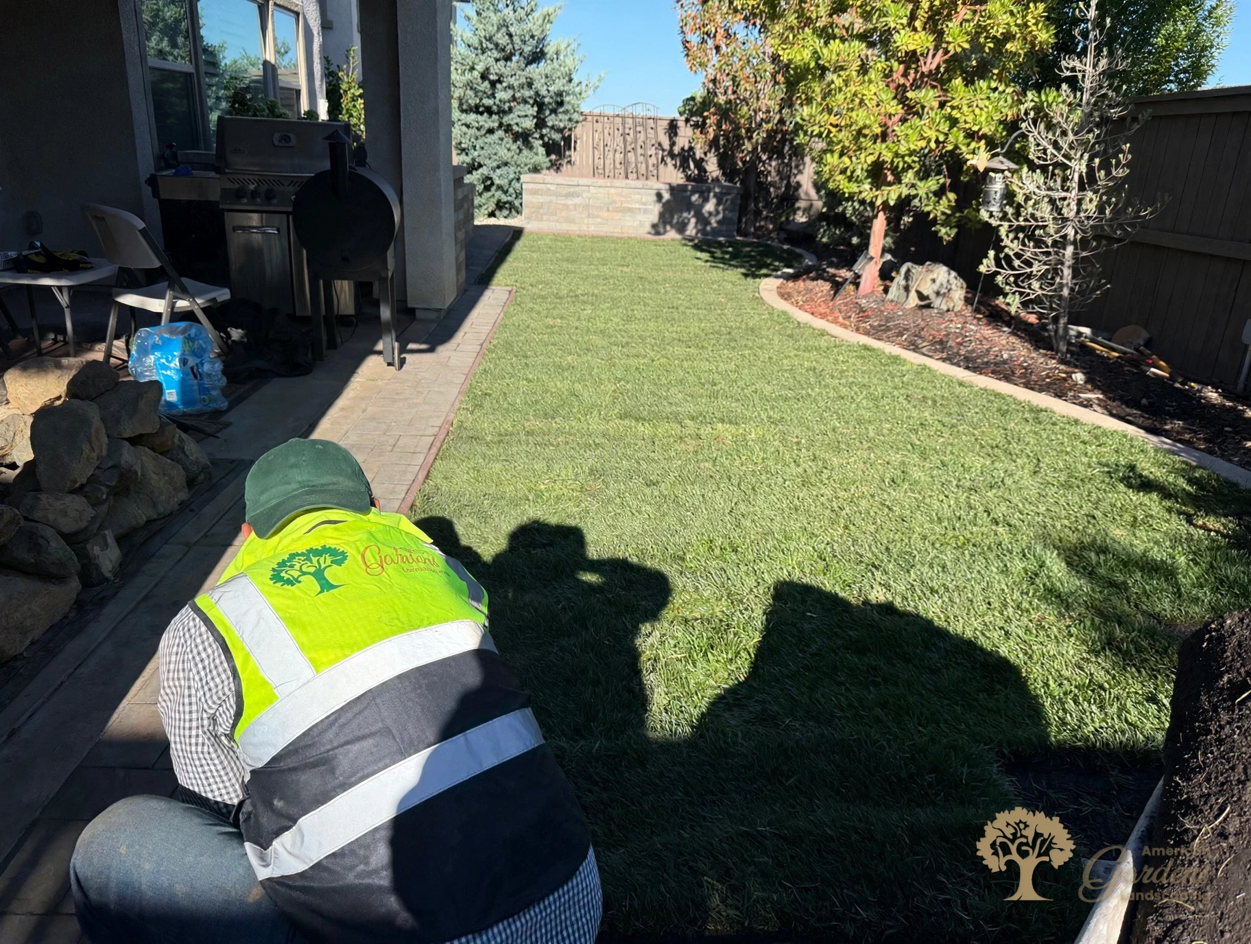 An American Gardens Landscaping crew member kneeling to finish the sod edge along the paver walkway in a Serrano backyard in El Dorado Hills.