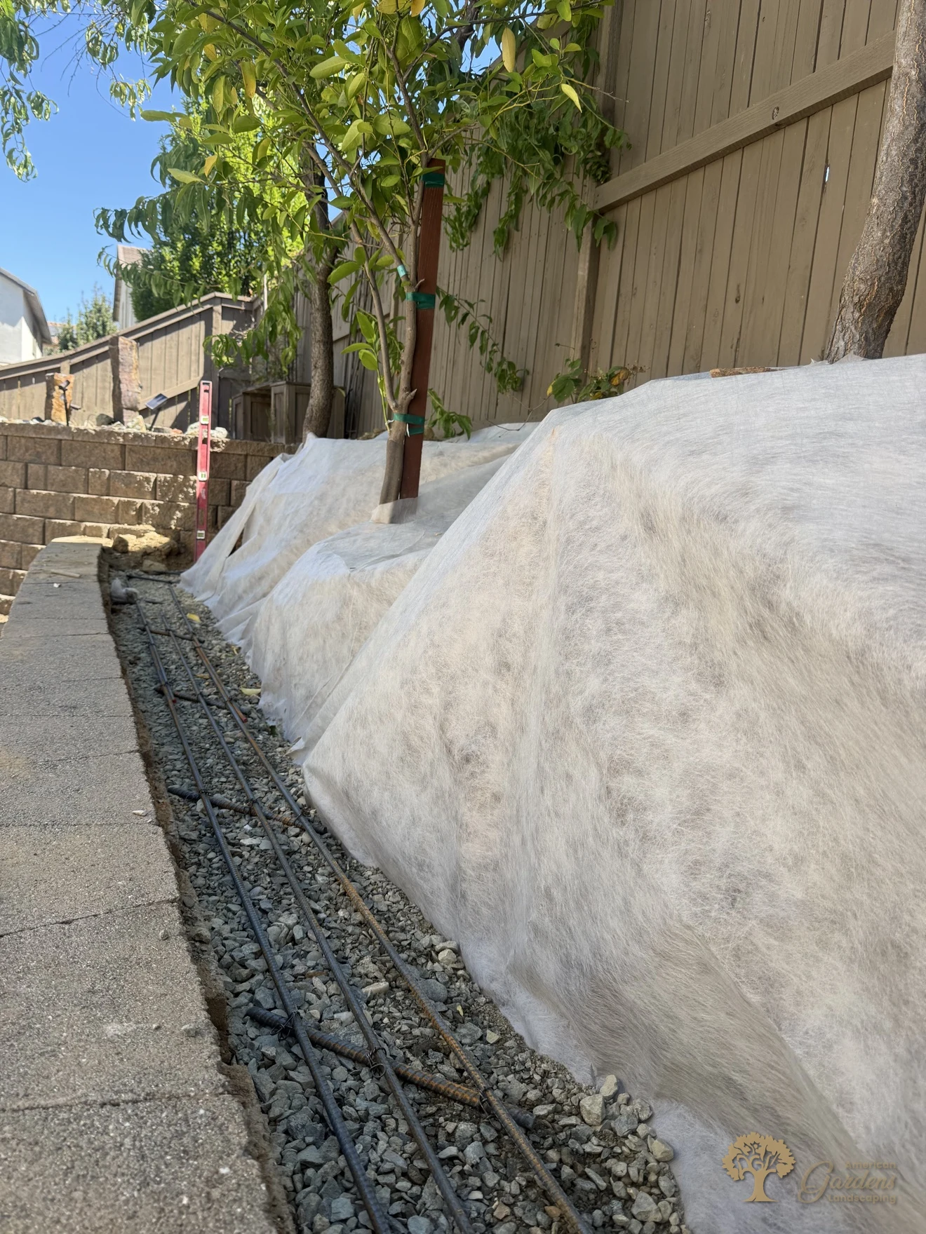 Steel rebar grid set in a gravel footing trench with filter fabric over the slope — the hidden strength of a new block retaining wall in El Dorado Hills' Serrano neighborhood, by American Gardens Landscaping.