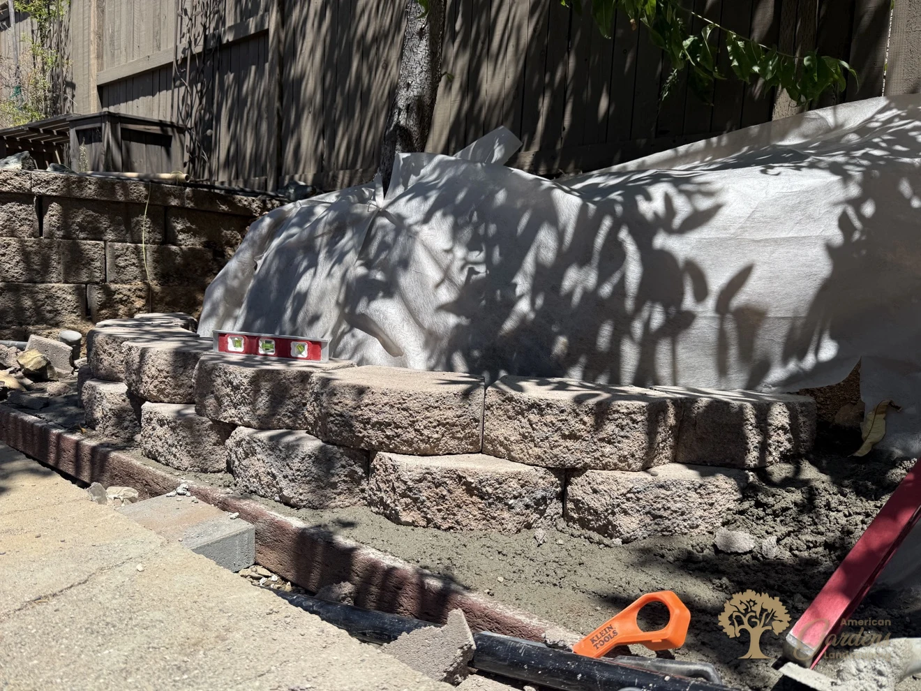 First courses of a block retaining wall being set level on their footing, with filter fabric protecting the slope behind, in El Dorado Hills, by American Gardens Landscaping.