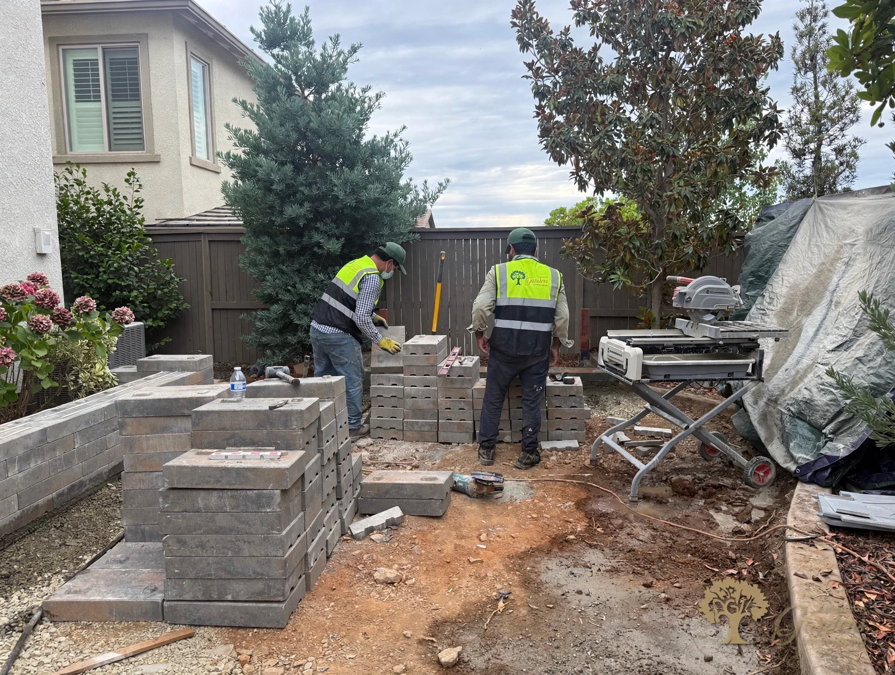 American Gardens Landscaping crew cutting and stacking retaining-wall blocks at the tile saw during a backyard build in El Dorado Hills' Serrano neighborhood.