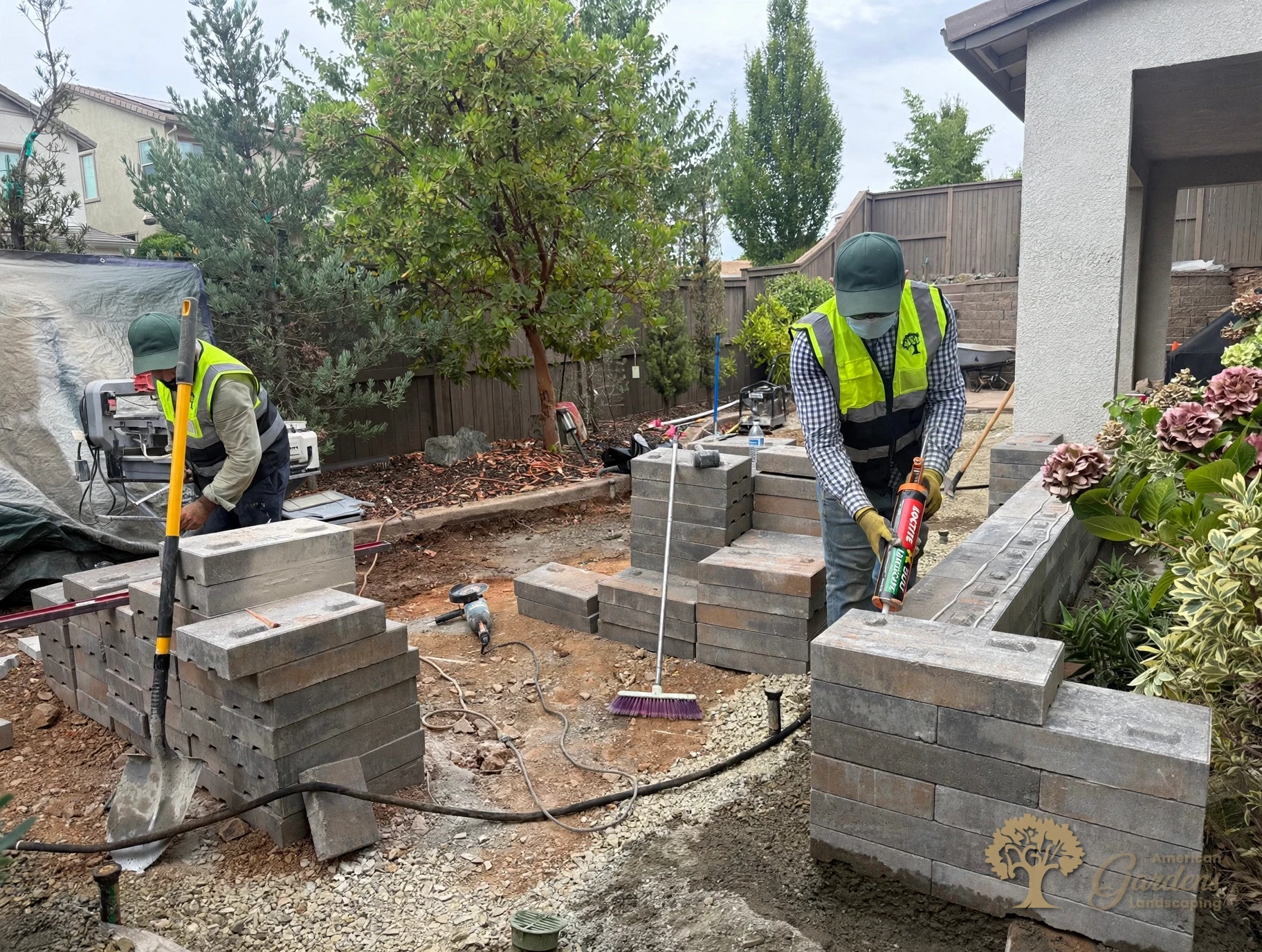 American Gardens Landscaping crew member applying construction adhesive to lock the capstones on a new raised bed wall in El Dorado Hills.