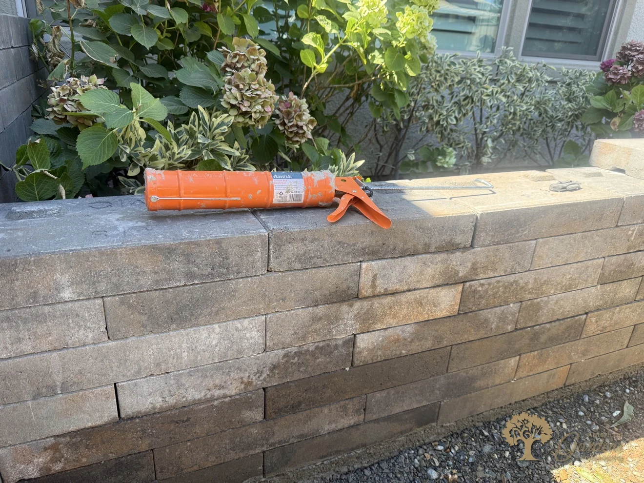 Finished capstones on a new raised planter wall, adhesive gun still on the wall, with hydrangeas behind in El Dorado Hills, by American Gardens Landscaping.