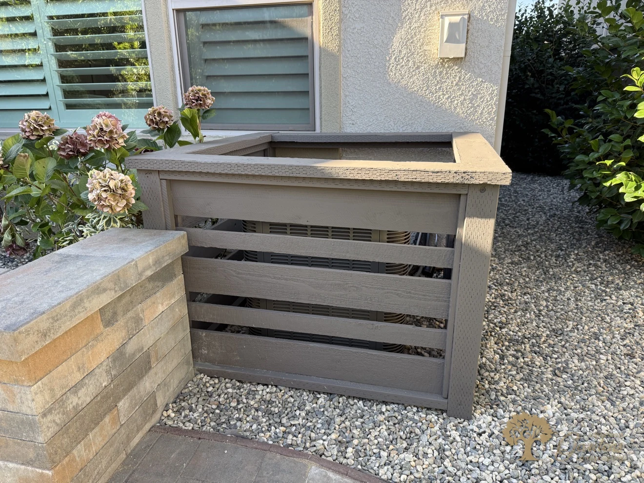 A stained slatted screen enclosure built around the AC unit, set in decorative gravel beside the new planter wall in El Dorado Hills, by American Gardens Landscaping.