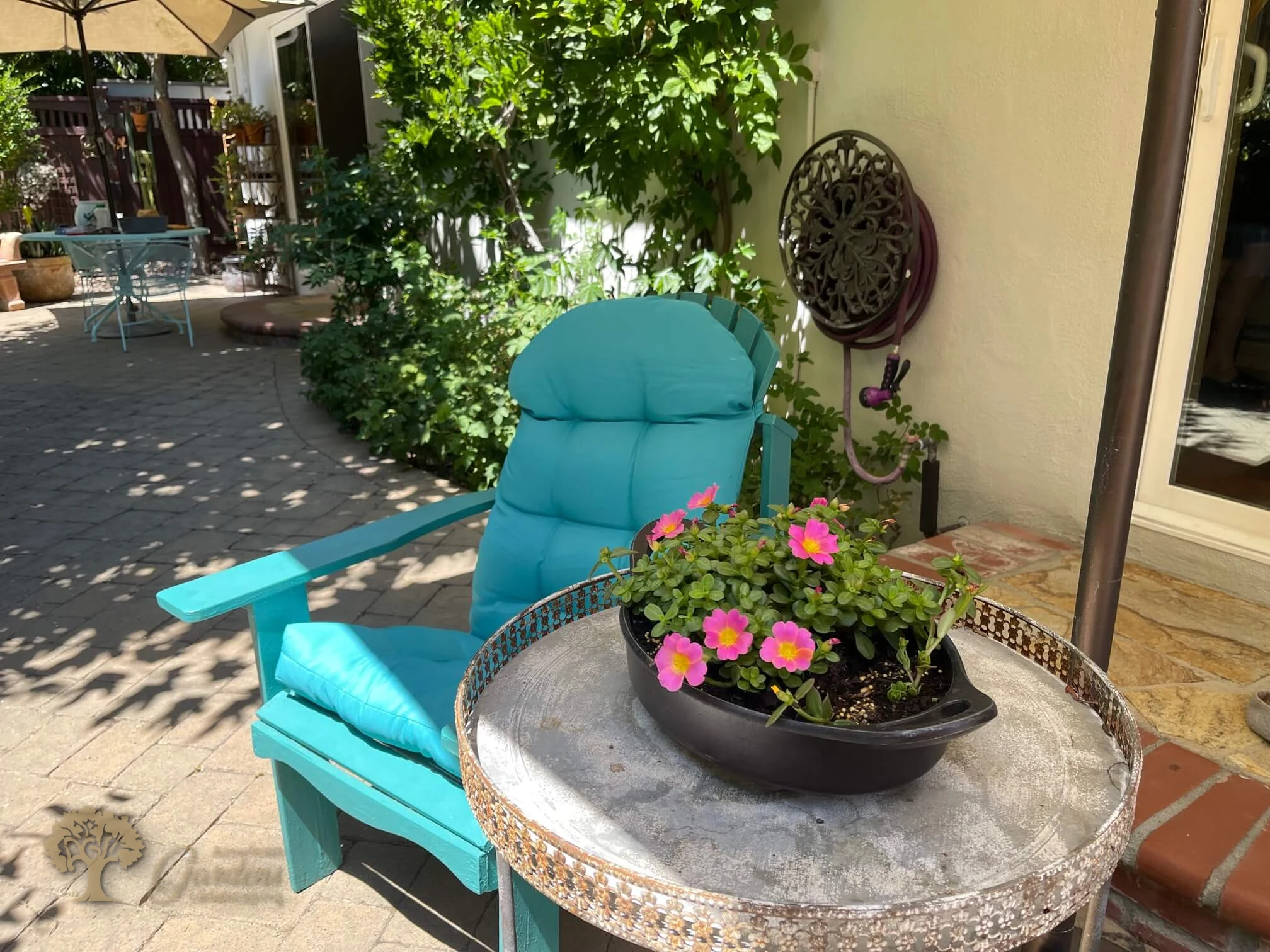 Potted container garden arrangement by American Gardens Landscaping — pink flowers in a planter on a patio table beside a turquoise chair