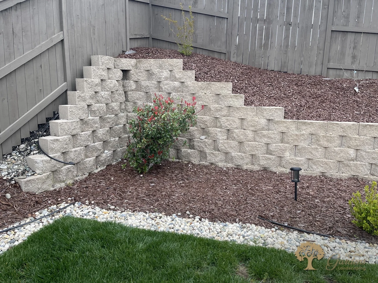 Stepped concrete block retaining wall with bark mulch beds, river rock swale and new plantings in a Rocklin backyard