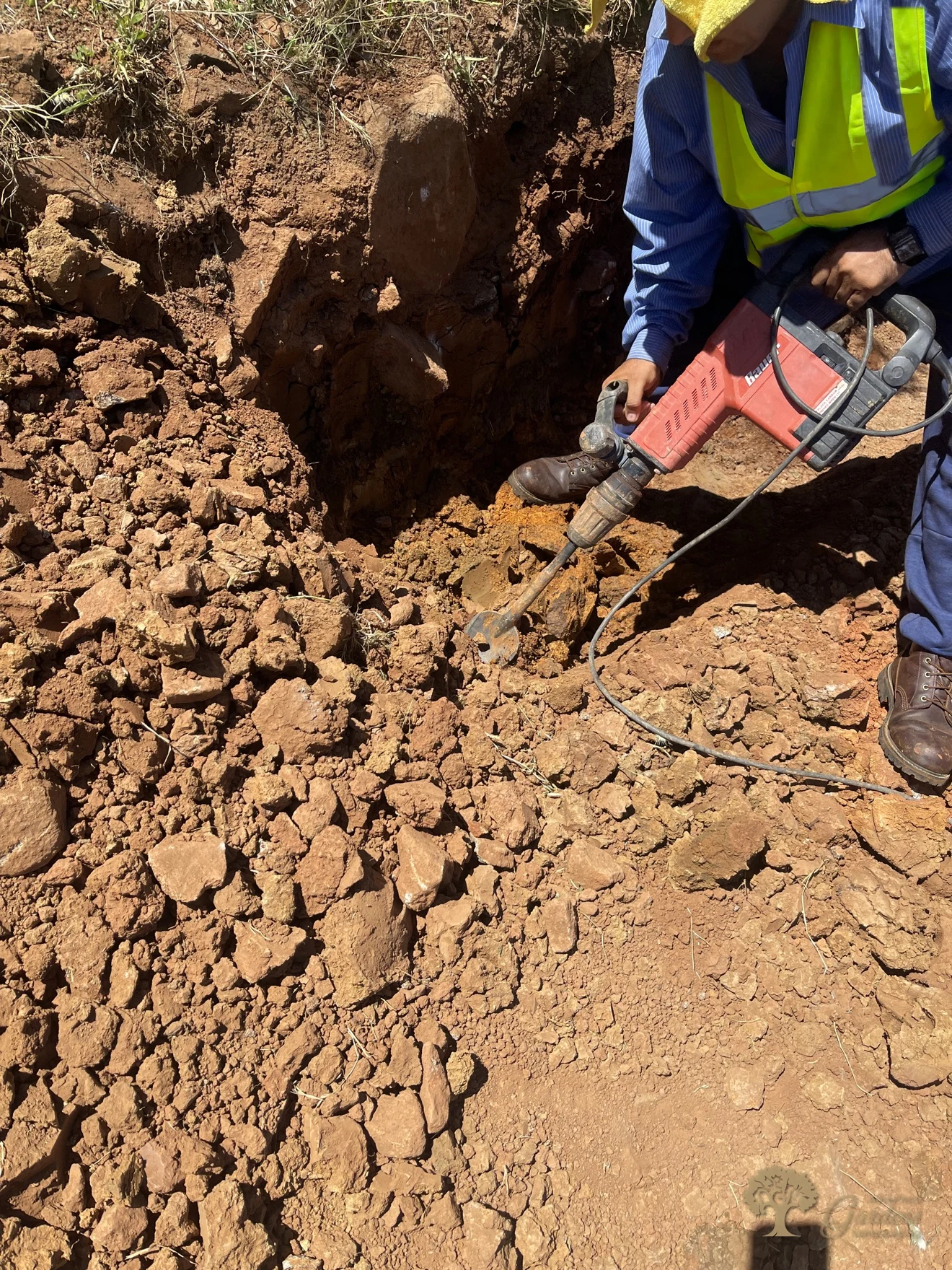 Worker breaking rock with a jackhammer while excavating a retaining wall trench in Shingle Springs