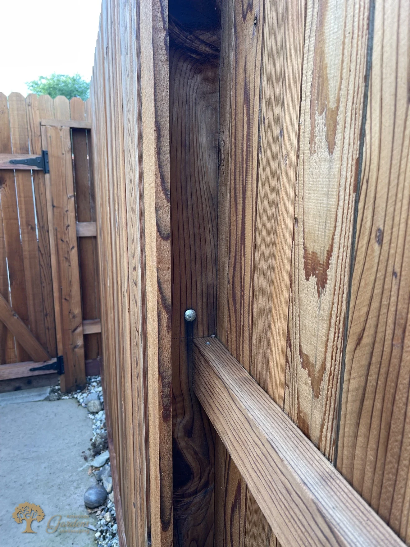Close-up detail of a fence post and rail joint secured with a lag bolt on a stained vertical-board fence by American Gardens Landscaping
