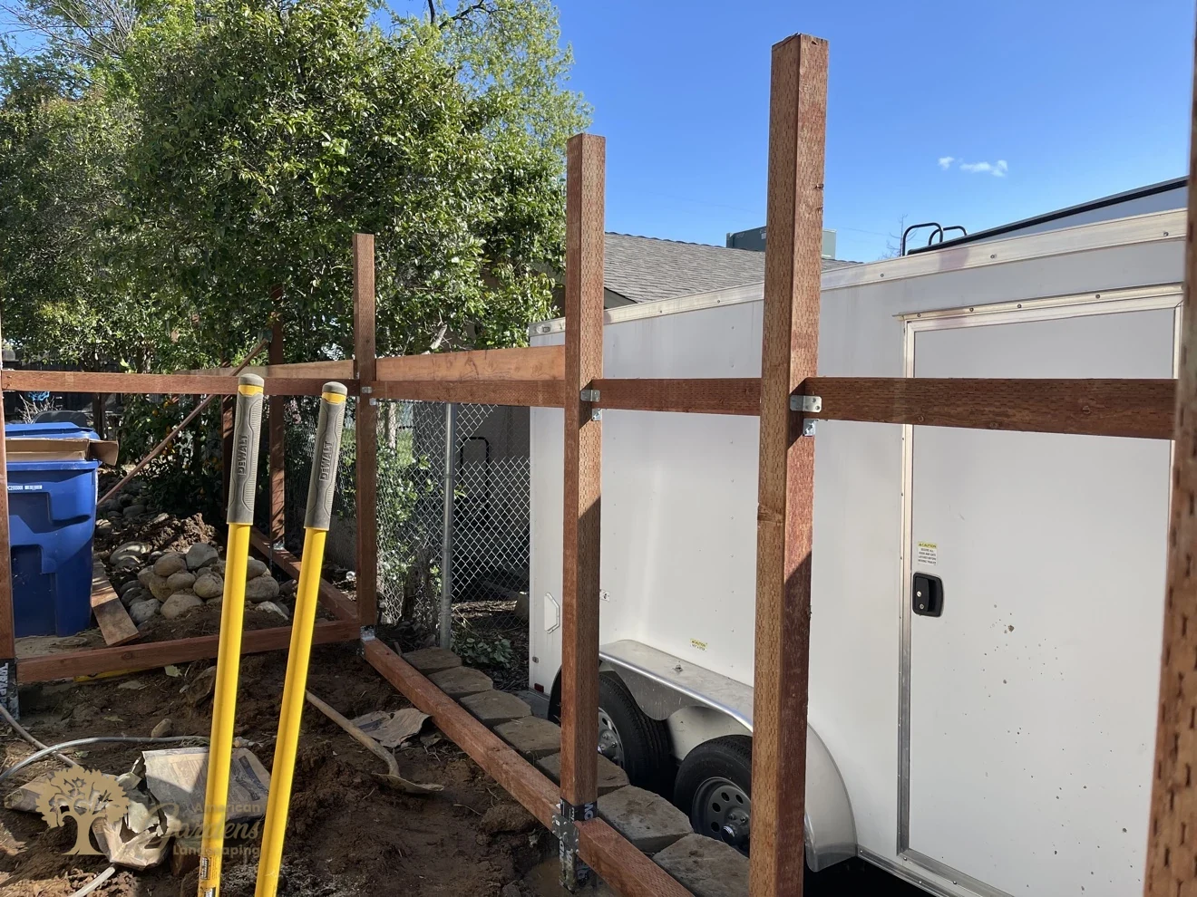 Fence rails mounted on Simpson brackets between posts with black post-wrap at the base, during a horizontal board fence installation by American Gardens Landscaping