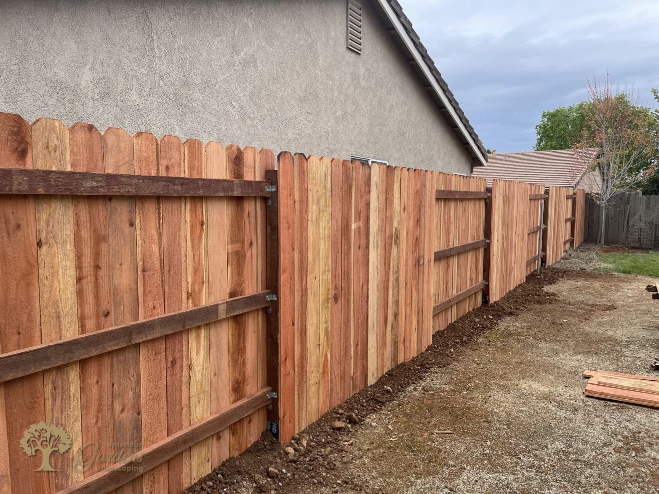 Fresh vertical redwood dog-ear fence with three pressure-treated rails running along the side of a house, built by American Gardens Landscaping