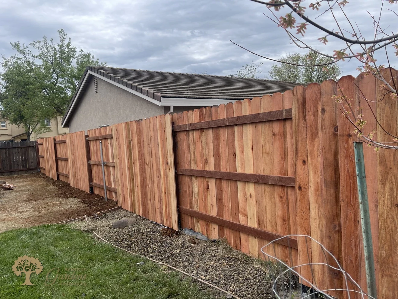 Long run of a fresh redwood dog-ear fence with three pressure-treated rails along a backyard, built by American Gardens Landscaping