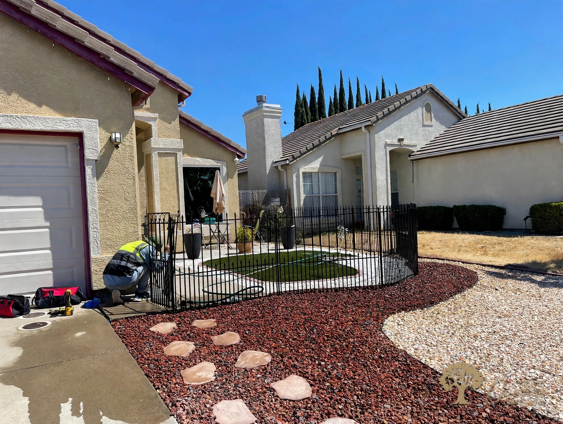 American Gardens Landscaping crew member installing a short black metal fence and gate around a front patio with a two-tone gravel xeriscape yard in Sacramento