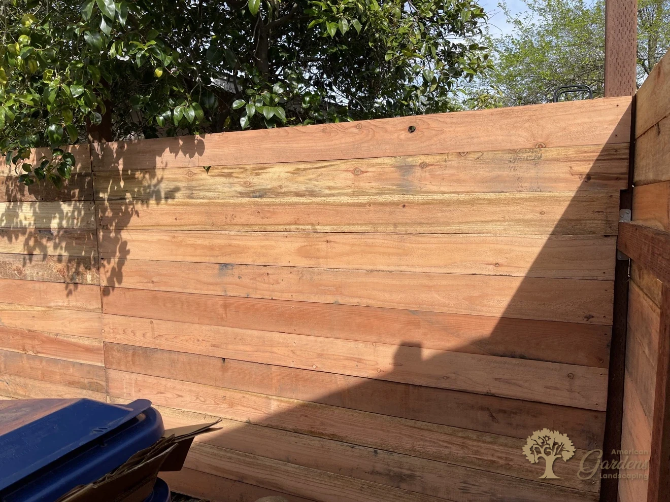 Finished horizontal redwood board fence at a backyard corner with a cap rail, built by American Gardens Landscaping