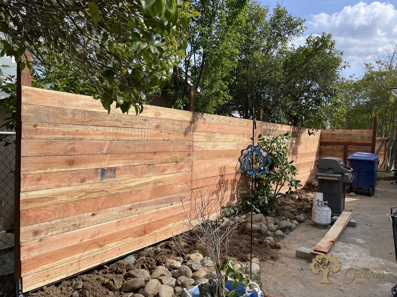 Finished horizontal redwood board fence along a boulder-edged garden bed in a backyard, built by American Gardens Landscaping