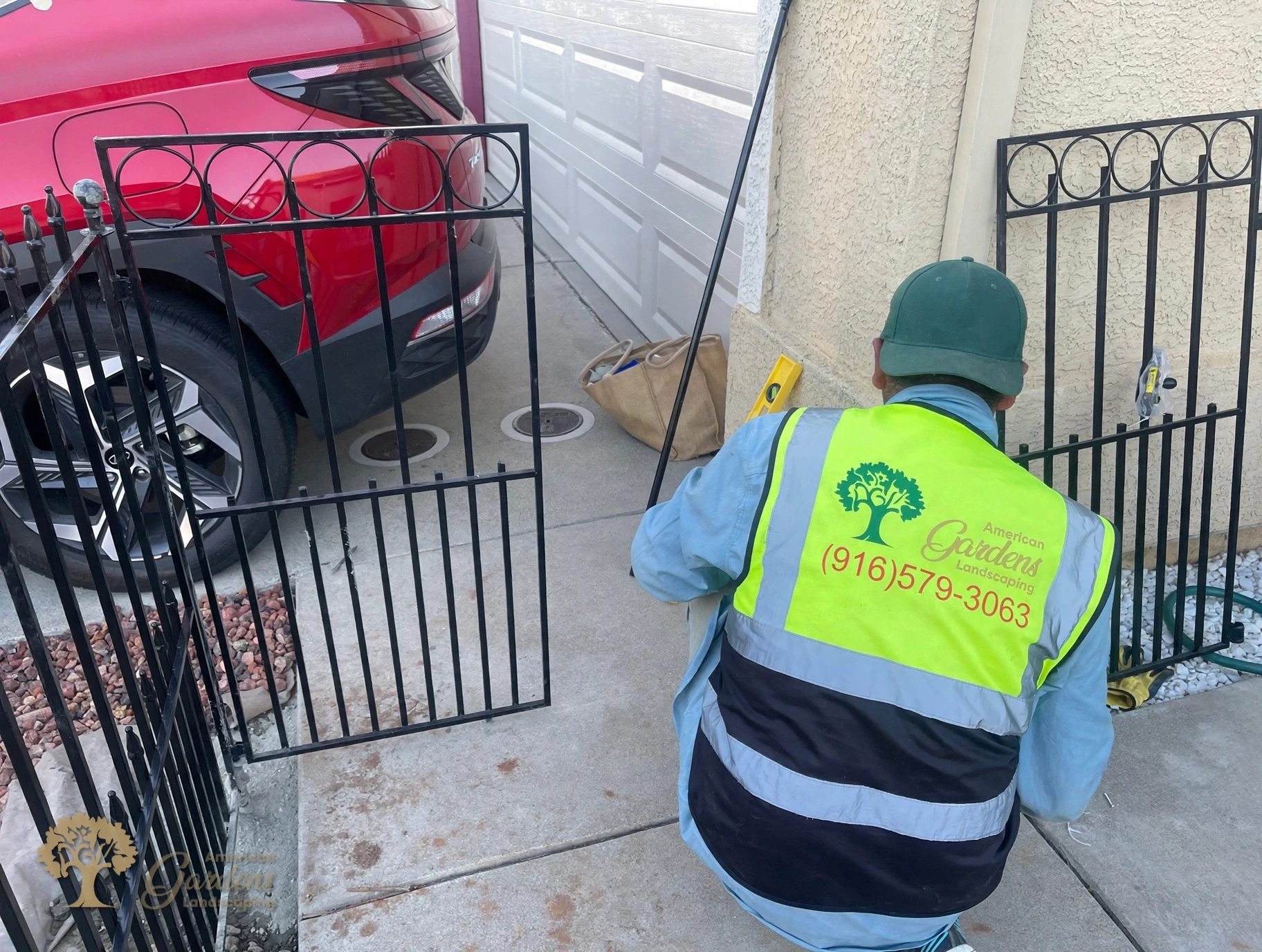 American Gardens Landscaping crew member in a company vest installing a black metal gate panel by a garage in Sacramento