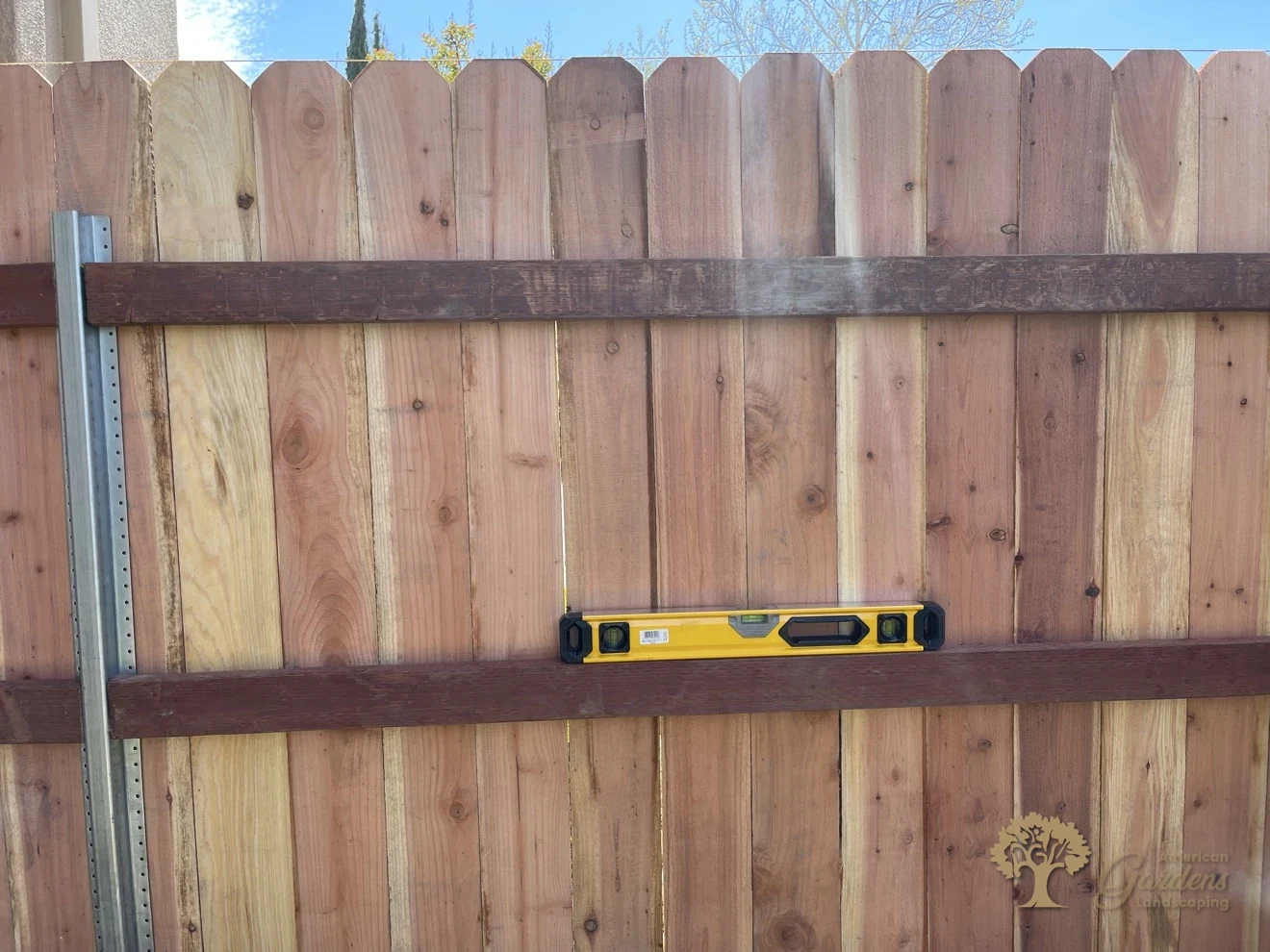 A yellow level resting on the rail of a redwood dog-ear fence on a steel post, checking the build for straightness in Roseville by American Gardens Landscaping