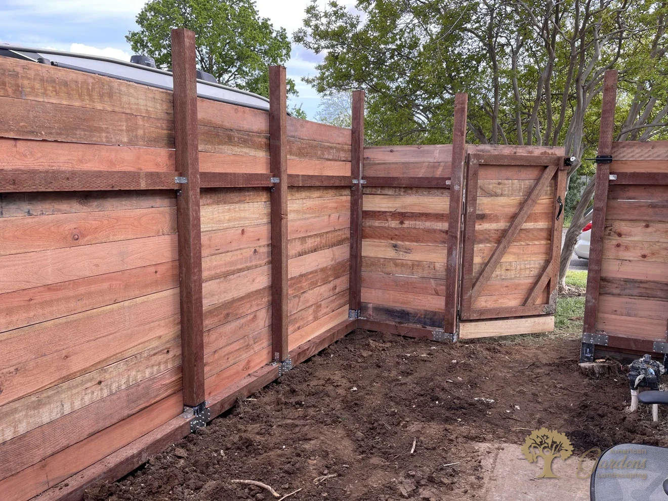 Back side of a horizontal redwood fence with a Z-braced gate, posts on black base brackets and Simpson steel connectors, built by American Gardens Landscaping