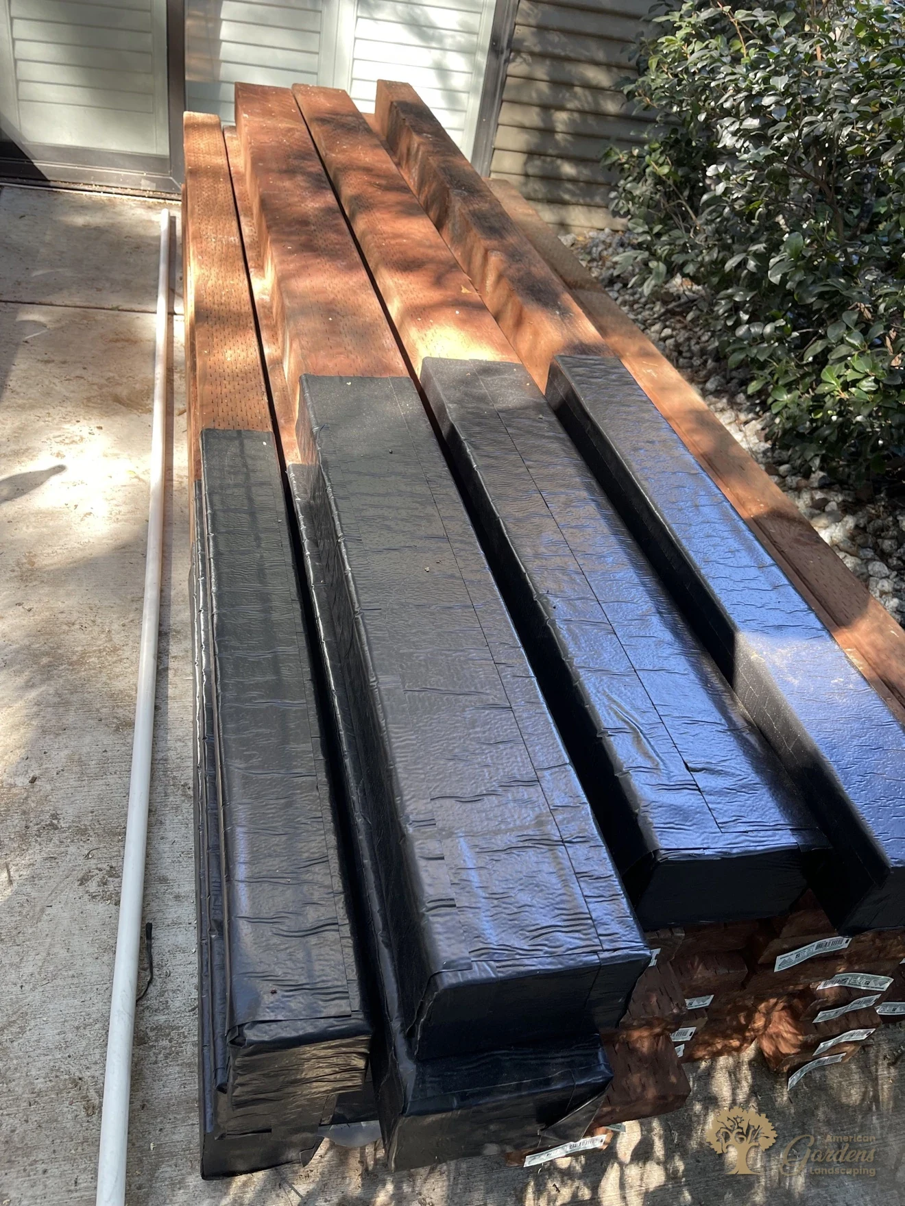 Close-up of new fence posts pre-wrapped in black waterproof post wrap stacked in Sacramento, ready for installation by American Gardens Landscaping