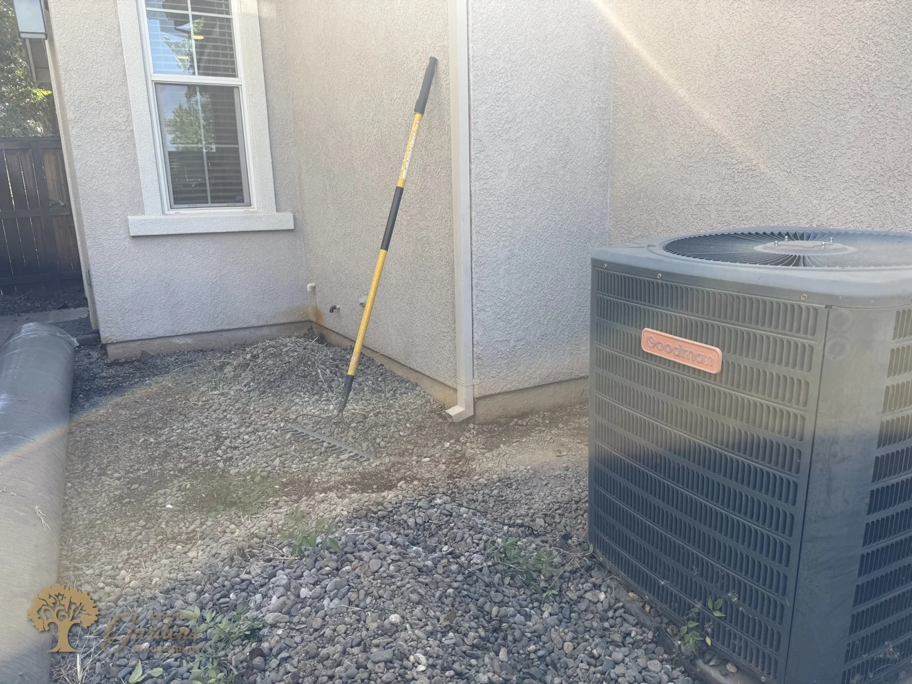 The worn river-rock side yard beside the AC unit in Rocklin before its conversion to artificial turf by American Gardens Landscaping