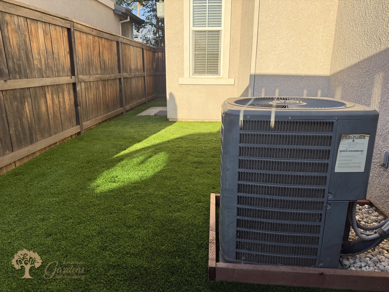 The finished green artificial turf running along the wooden fence beside the AC unit in a Rocklin side yard, by American Gardens Landscaping