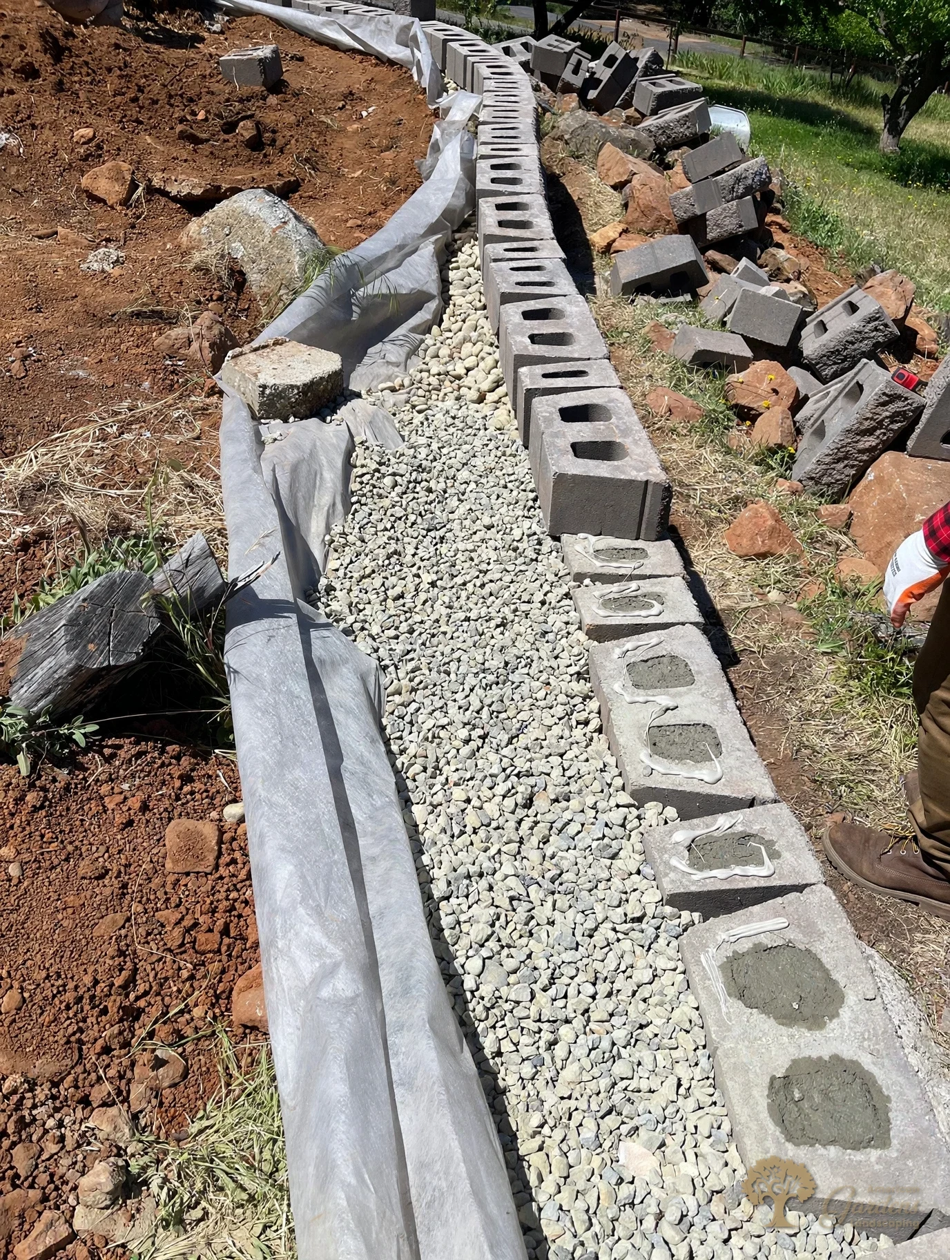 Filter fabric and drainage gravel behind a block retaining wall, with block cores being filled with concrete, by American Gardens Landscaping in the Sacramento area