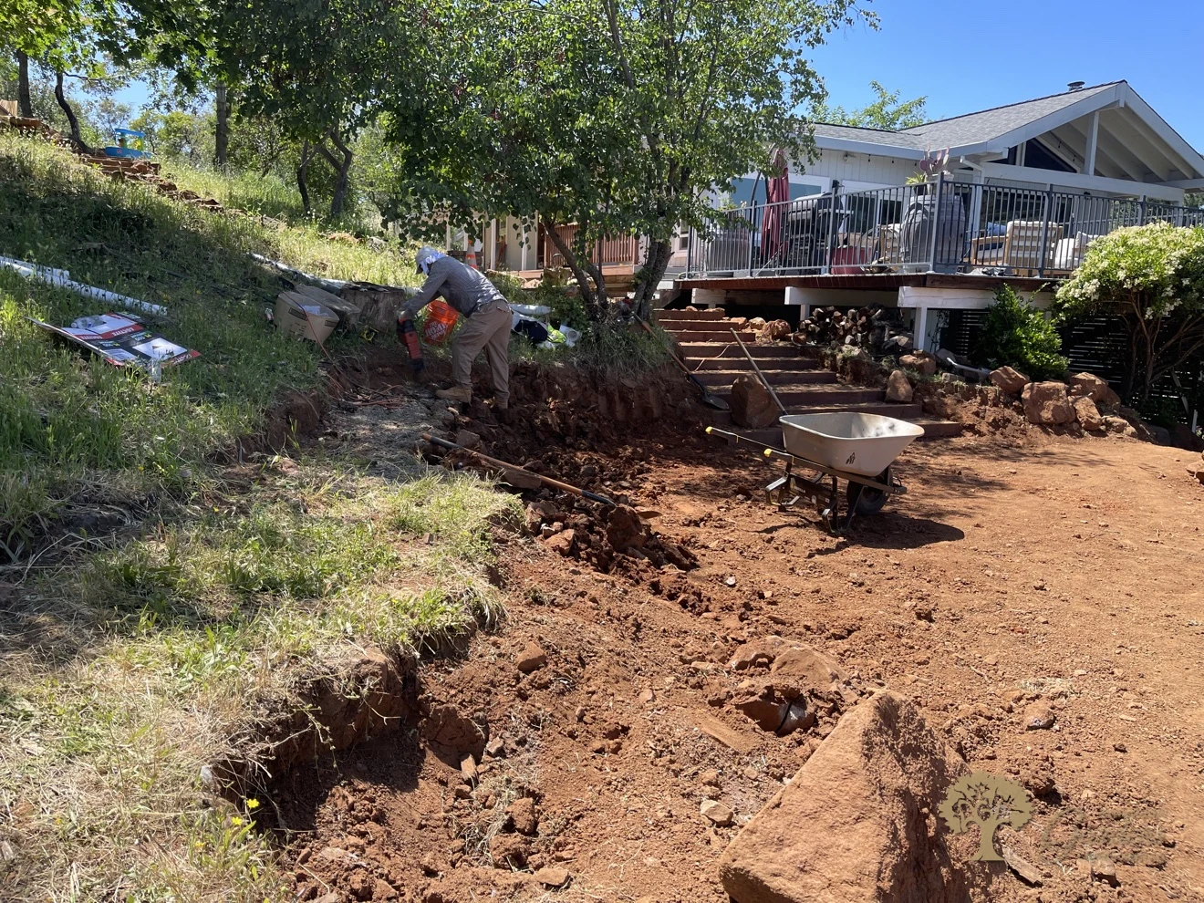 Crew excavating a hillside bench by hand below a house before building a retaining wall, by American Gardens Landscaping in the Sacramento area