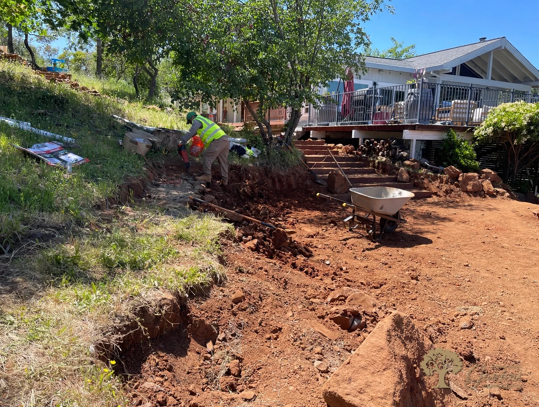 Crew excavating a hillside bench by hand below a house before building a retaining wall, by American Gardens Landscaping in the Sacramento area