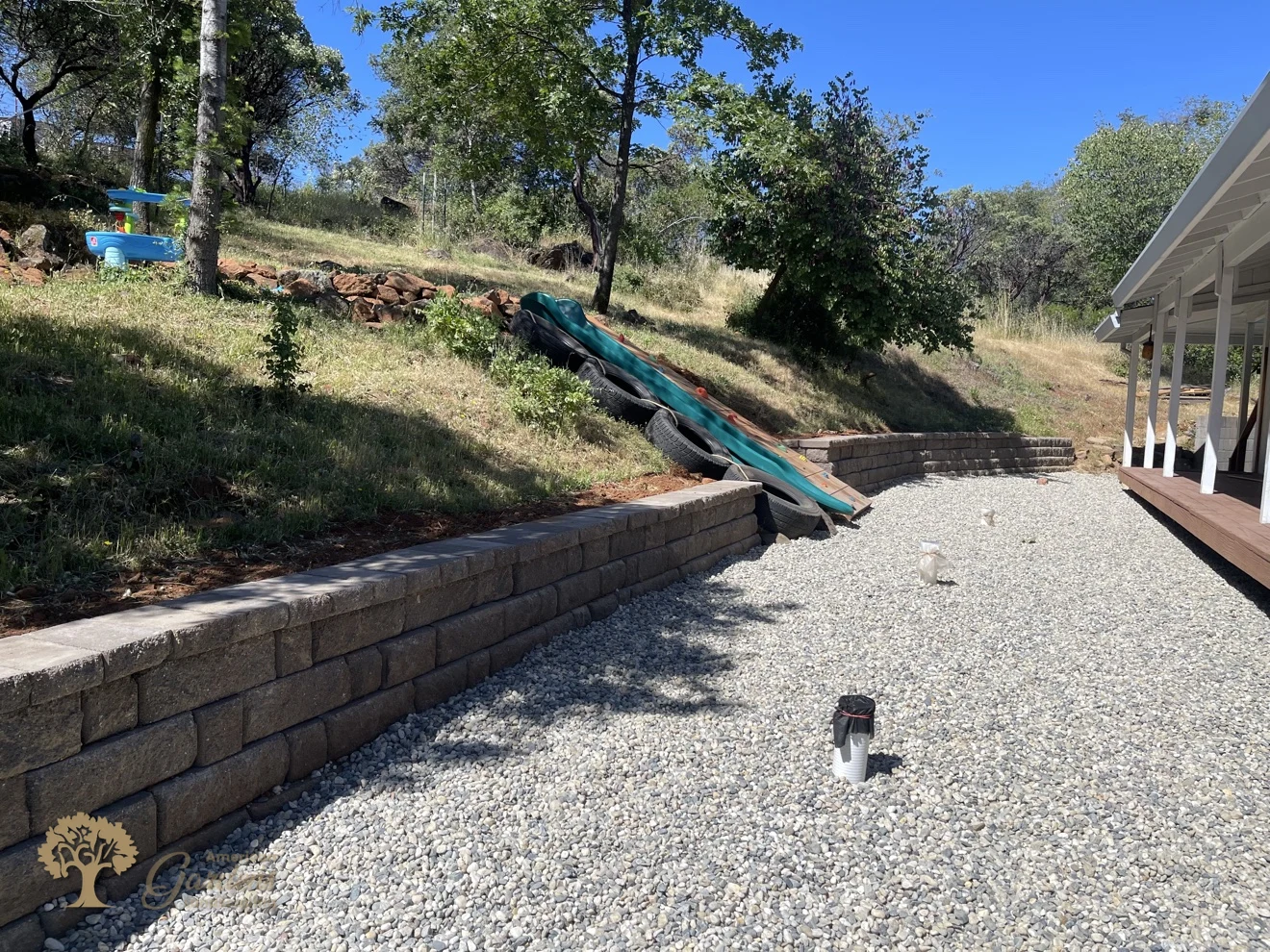 Finished long curved block retaining wall with capstones and a gravel yard beside a house, built by American Gardens Landscaping in the Sacramento area