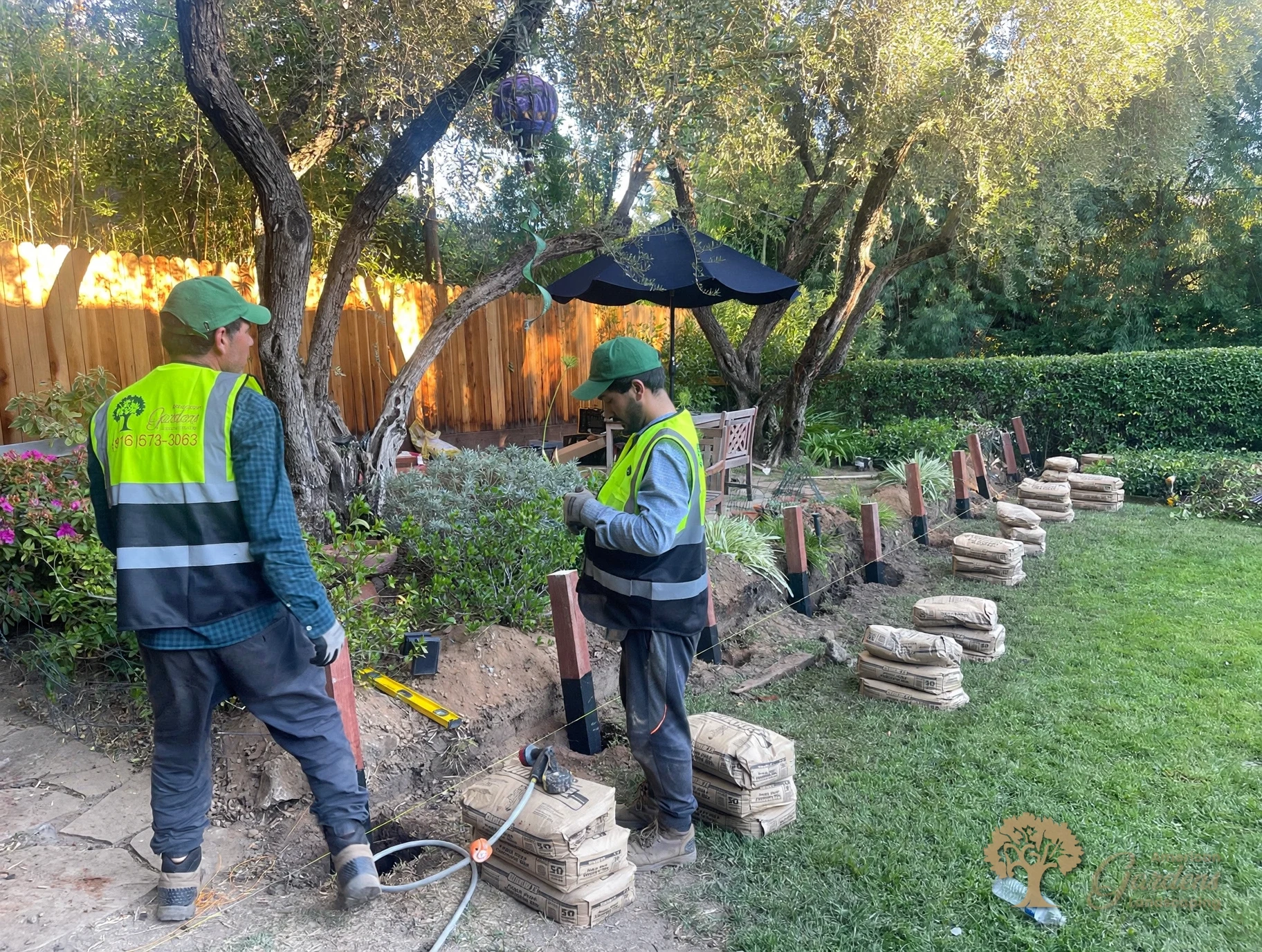 The new pressure-treated posts set in a row on the string line in Fair Oaks, their bases wrapped in black waterproof wrap and fence-post concrete bags stacked at each hole, by American Gardens Landscaping