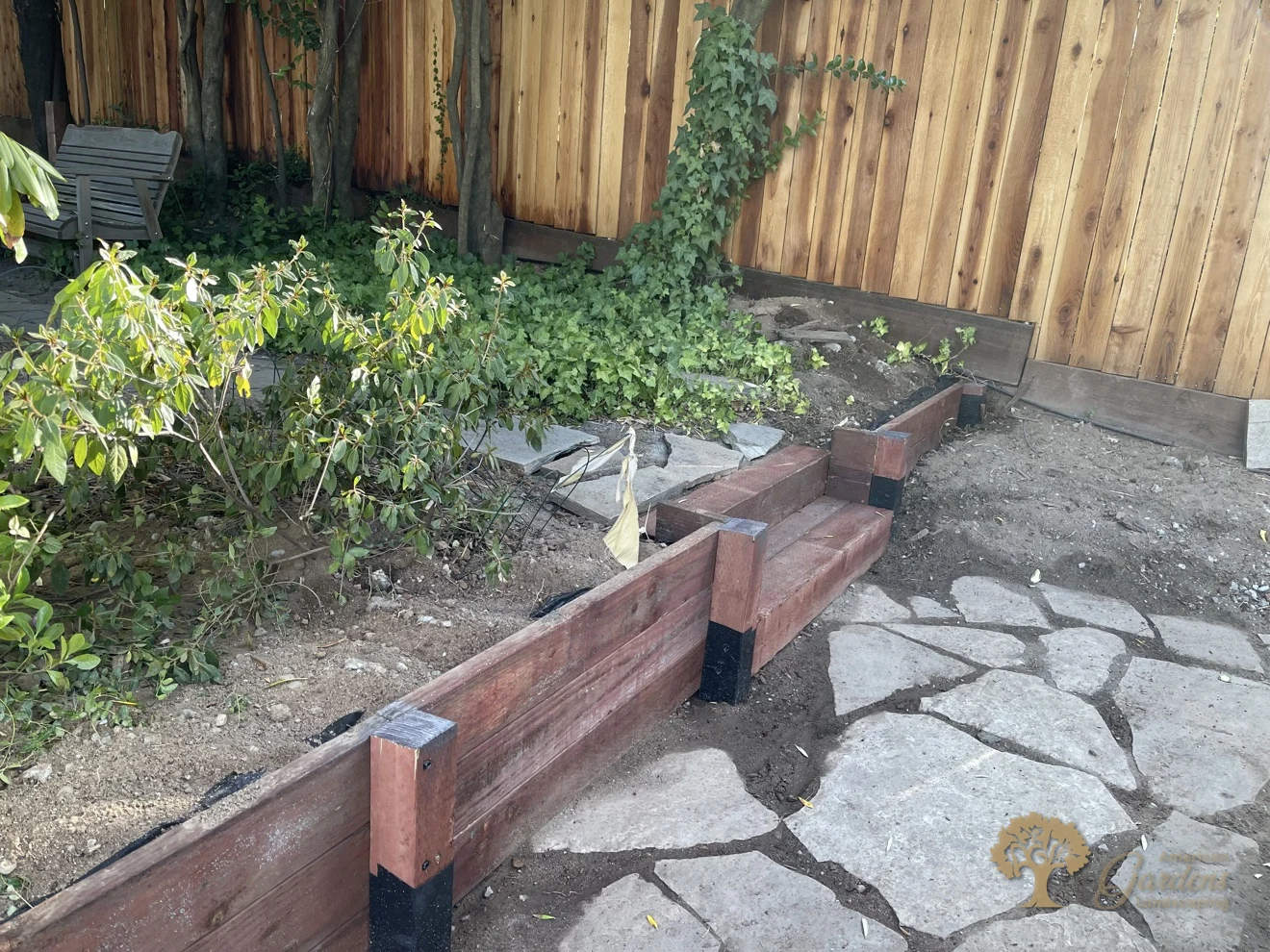 A stepped section of the new pressure-treated timber retaining wall stepping down to a flagstone patio in Fair Oaks, with waterproof post wrap on the post bases, by American Gardens Landscaping