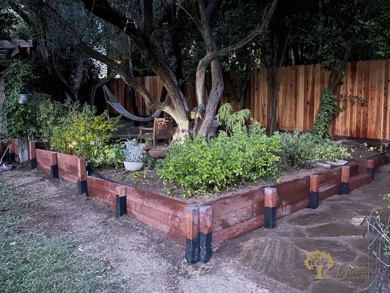 Finished pressure-treated timber retaining wall stepping down to a wet flagstone patio in Fair Oaks, with waterproof-wrapped post bases, built by American Gardens Landscaping