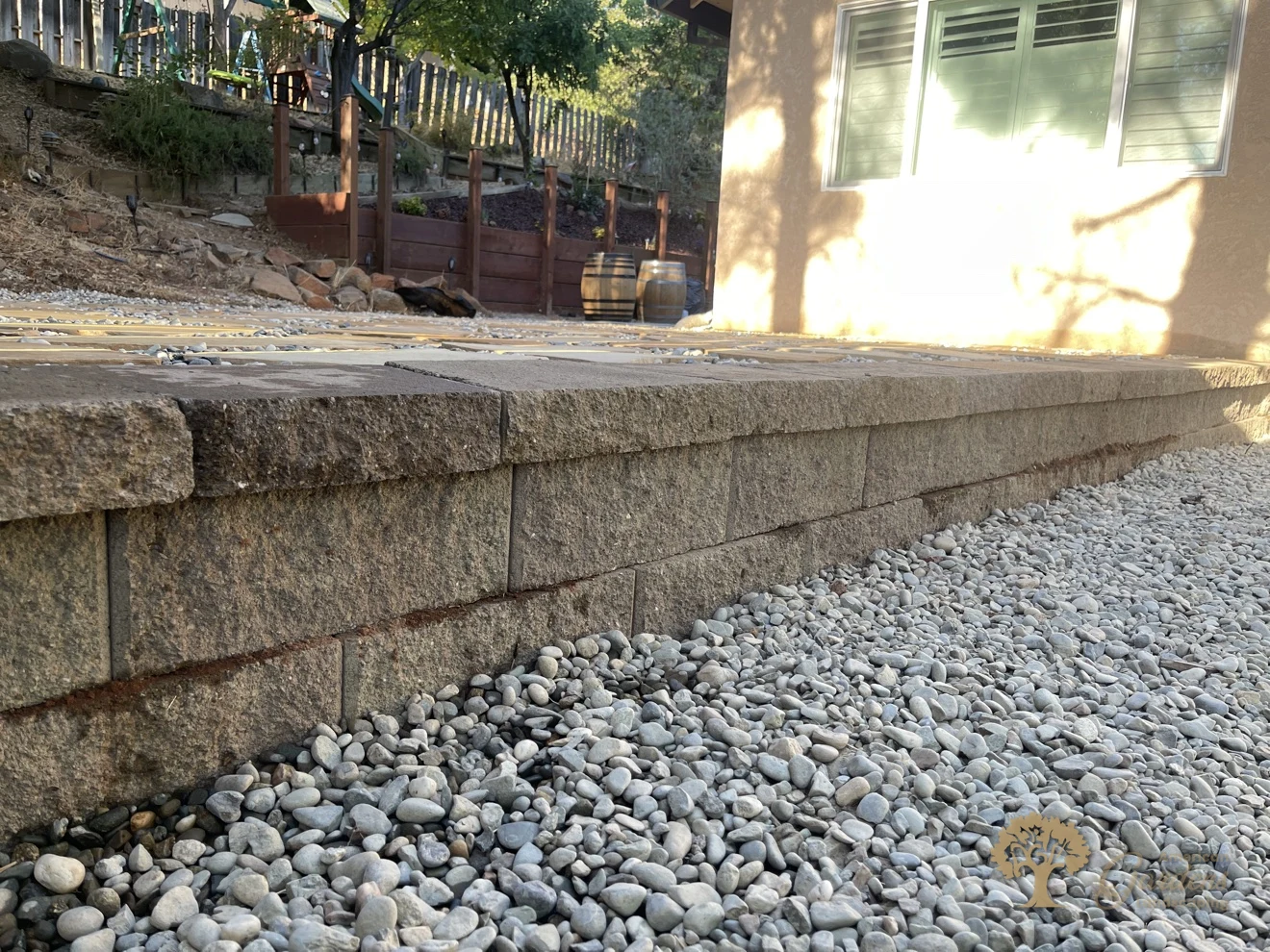 A low-angle close view of the finished concrete block retaining wall face with capstones and a pebble drainage bed in Shingle Springs, by American Gardens Landscaping