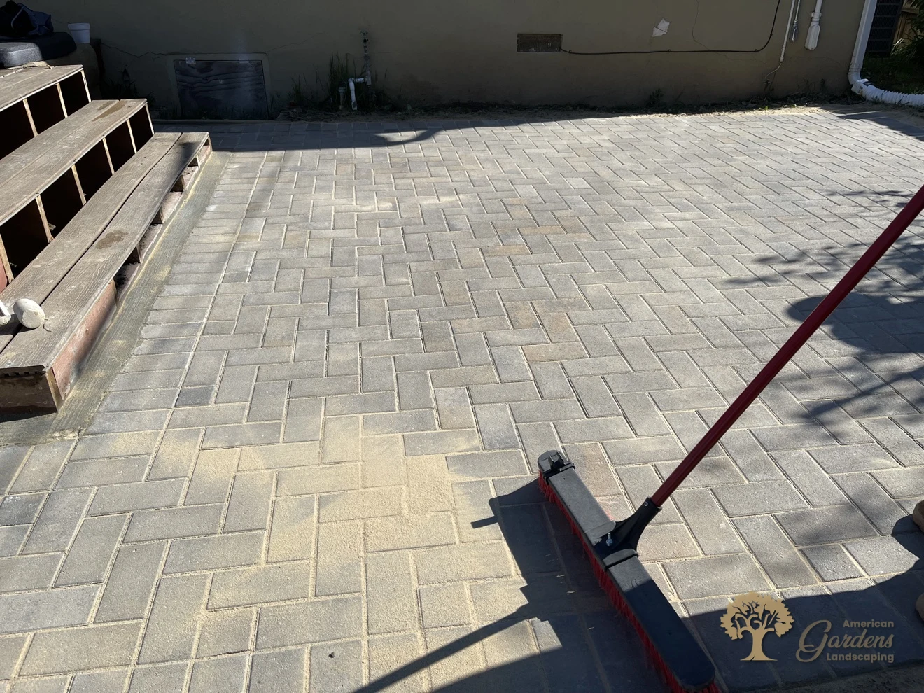Polymeric sand being swept into the joints of a herringbone paver patio in Sacramento – American Gardens Landscaping