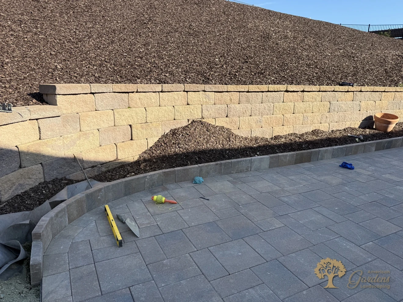 Close-up detail of a curved soldier-course paver border against a block retaining wall with a bark hillside in El Dorado Hills by American Gardens Landscaping