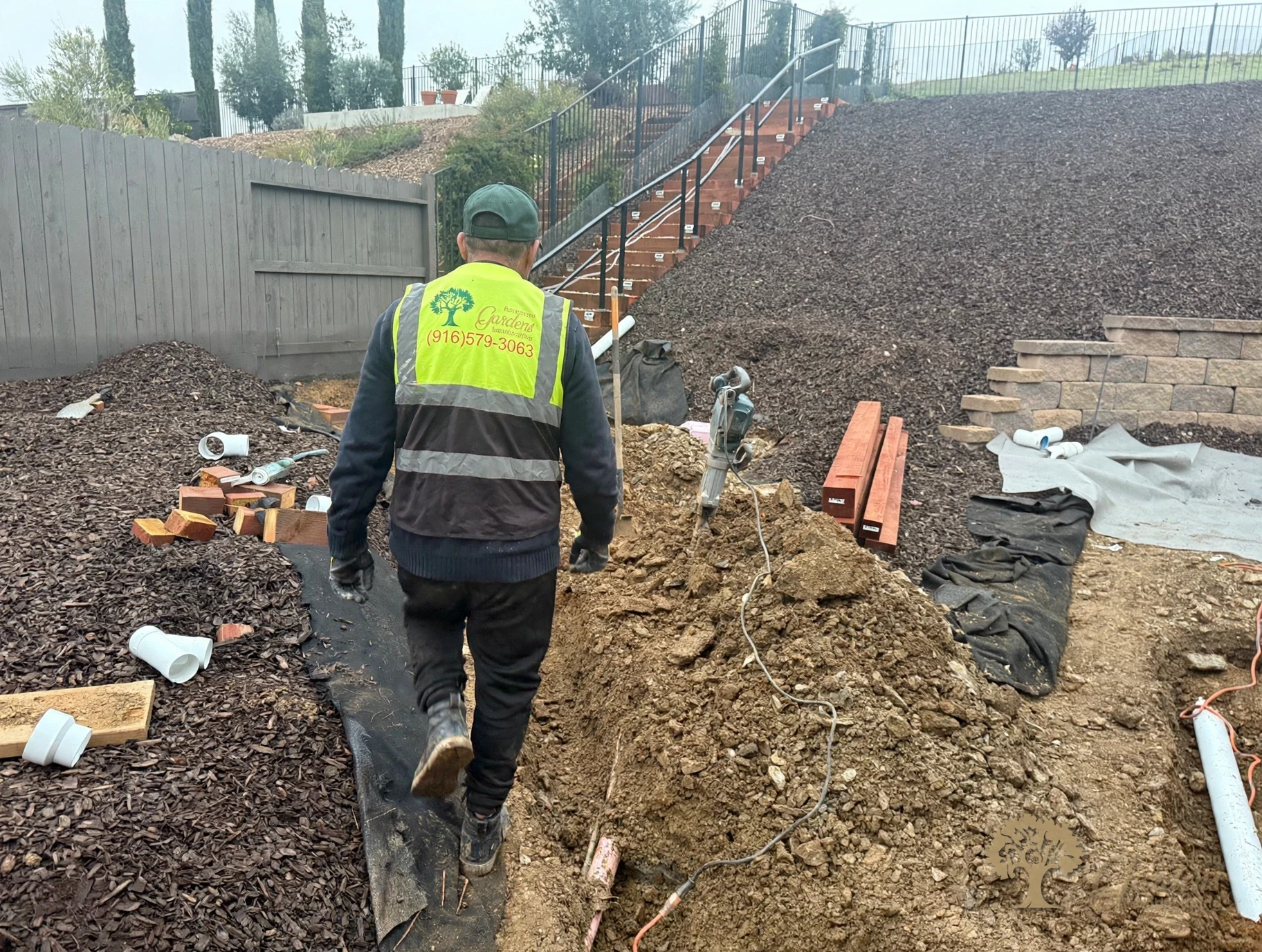 Early stage of a paver patio project in El Dorado Hills - geotextile fabric and drainage pipes on the graded yard, with an American Gardens Landscaping crew member at work