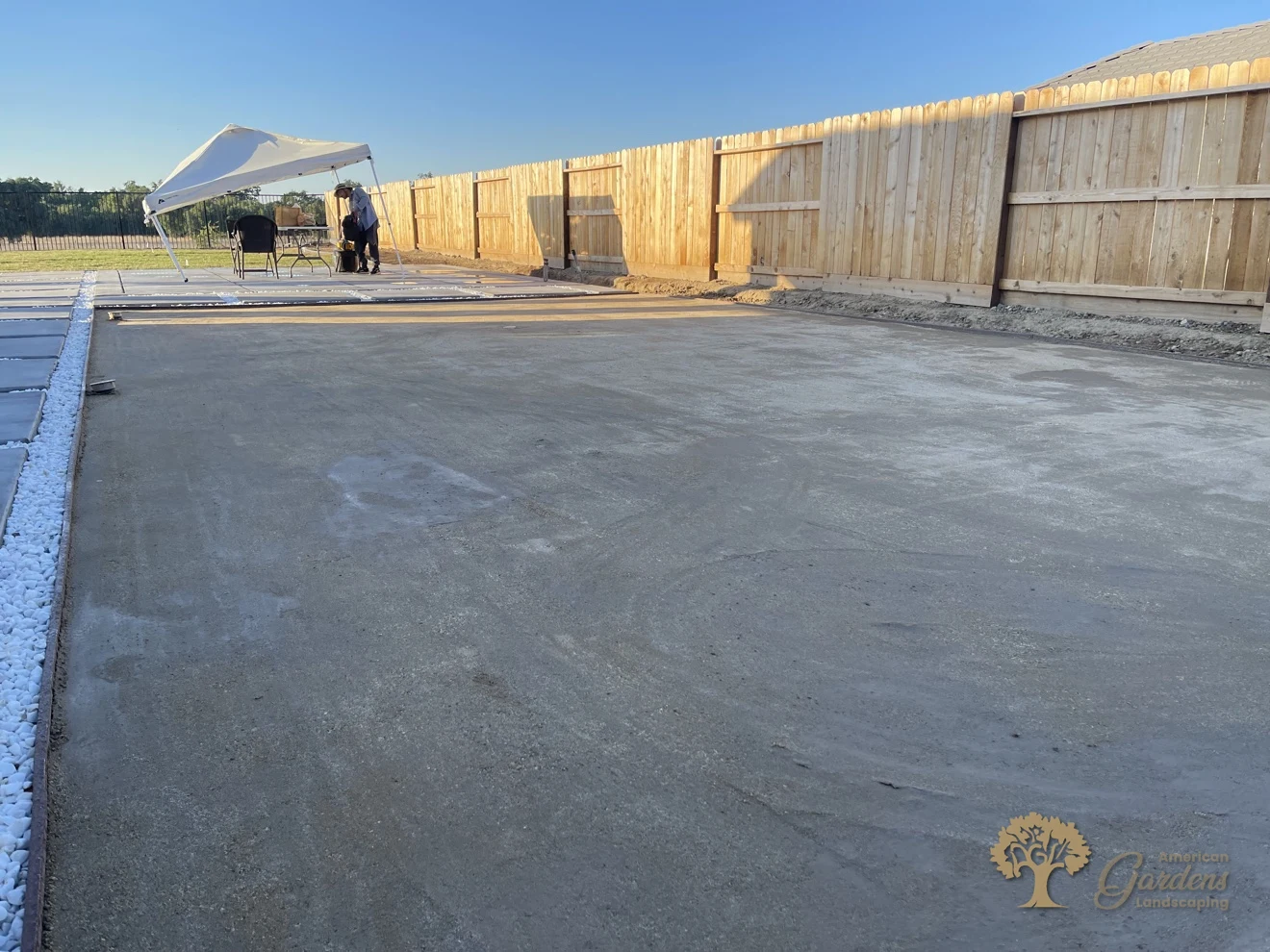 Finished smooth compacted decomposed granite pad beside concrete pavers with white-rock joints and a new wood fence, installed by American Gardens Landscaping