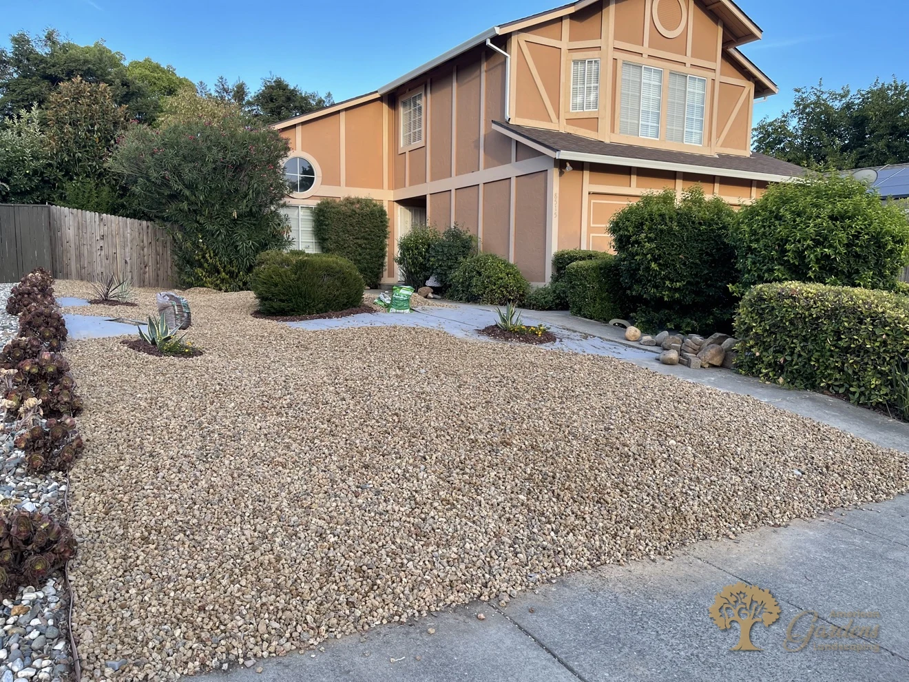 Finished decorative gravel xeriscape front yard with a succulent and river-rock border, seen from the driveway of a Tudor-style house in Rancho Cordova by American Gardens Landscaping