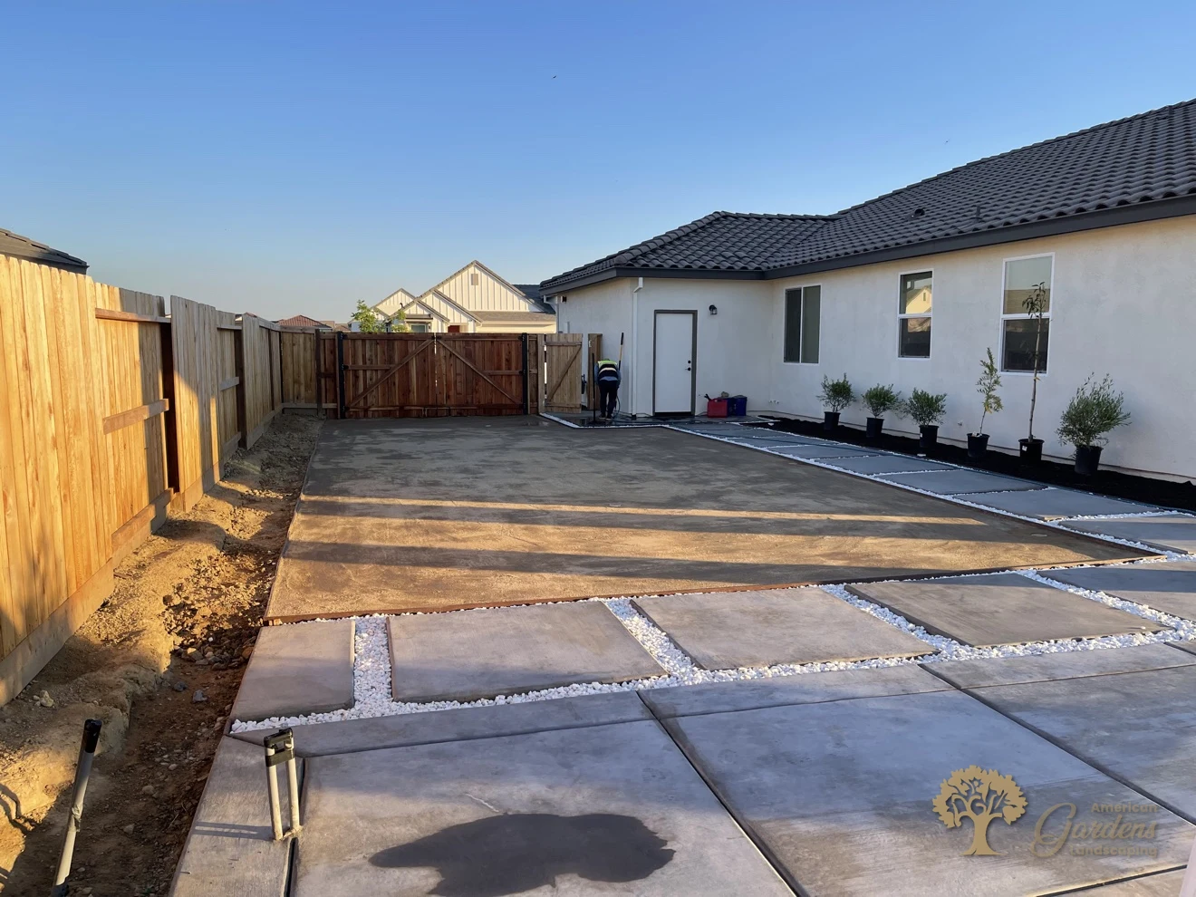Wide finished view of a compacted decomposed granite yard with concrete pavers, white-rock joints and potted olive trees along the house, installed by American Gardens Landscaping